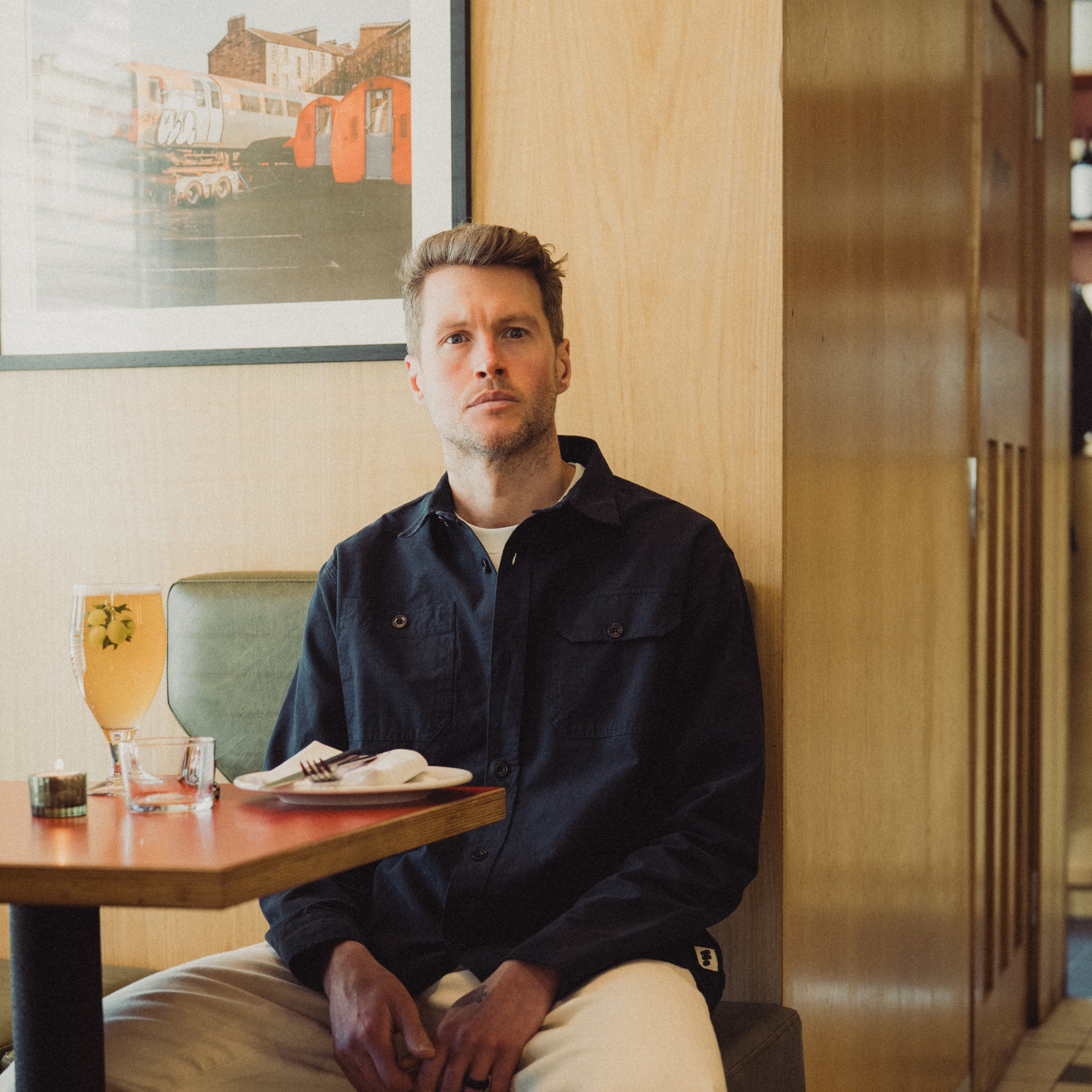 Man sitting at a table in a restaurant with a painting on the wall behind him.