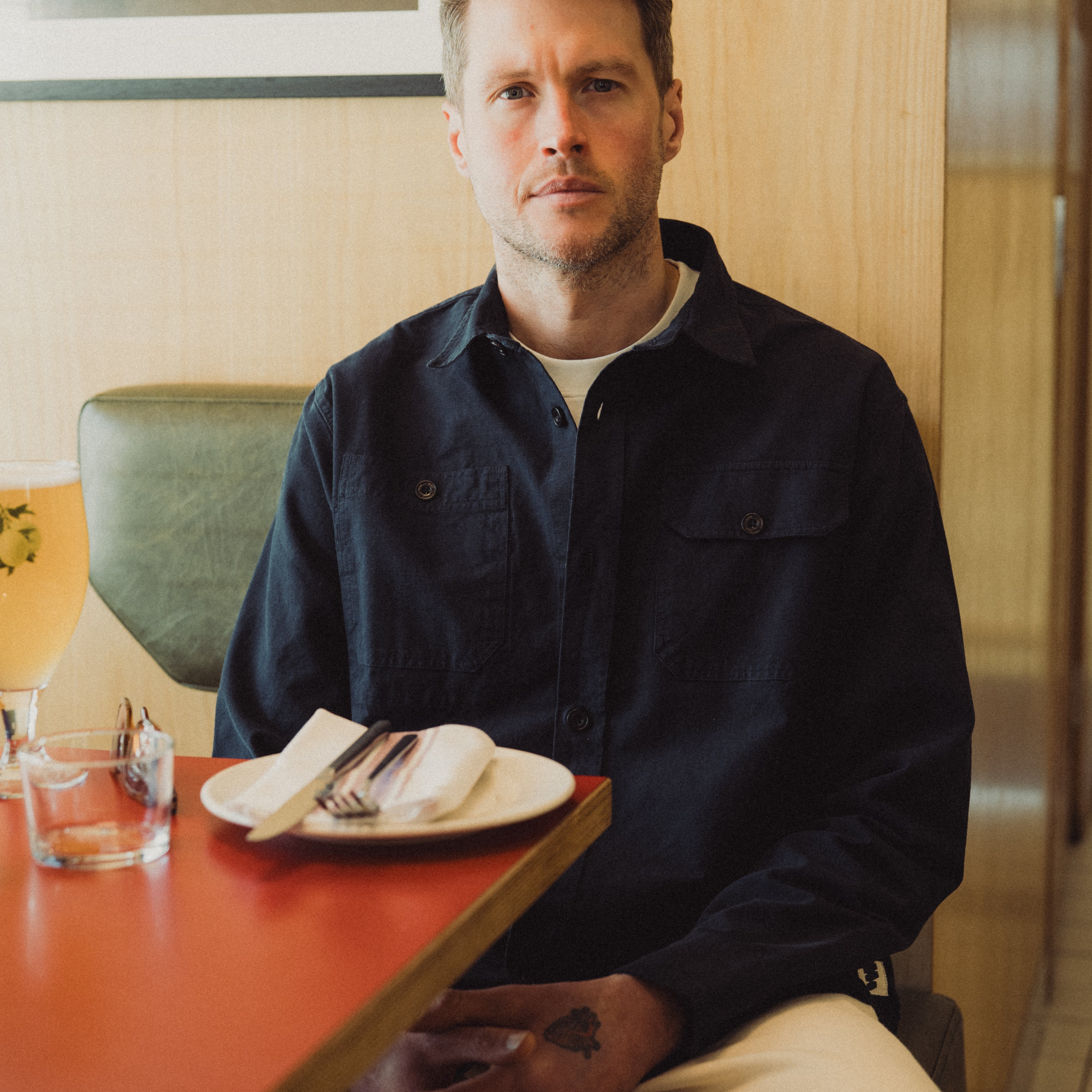 Man sitting at a table in a casual setting with a plate of food and a drink.