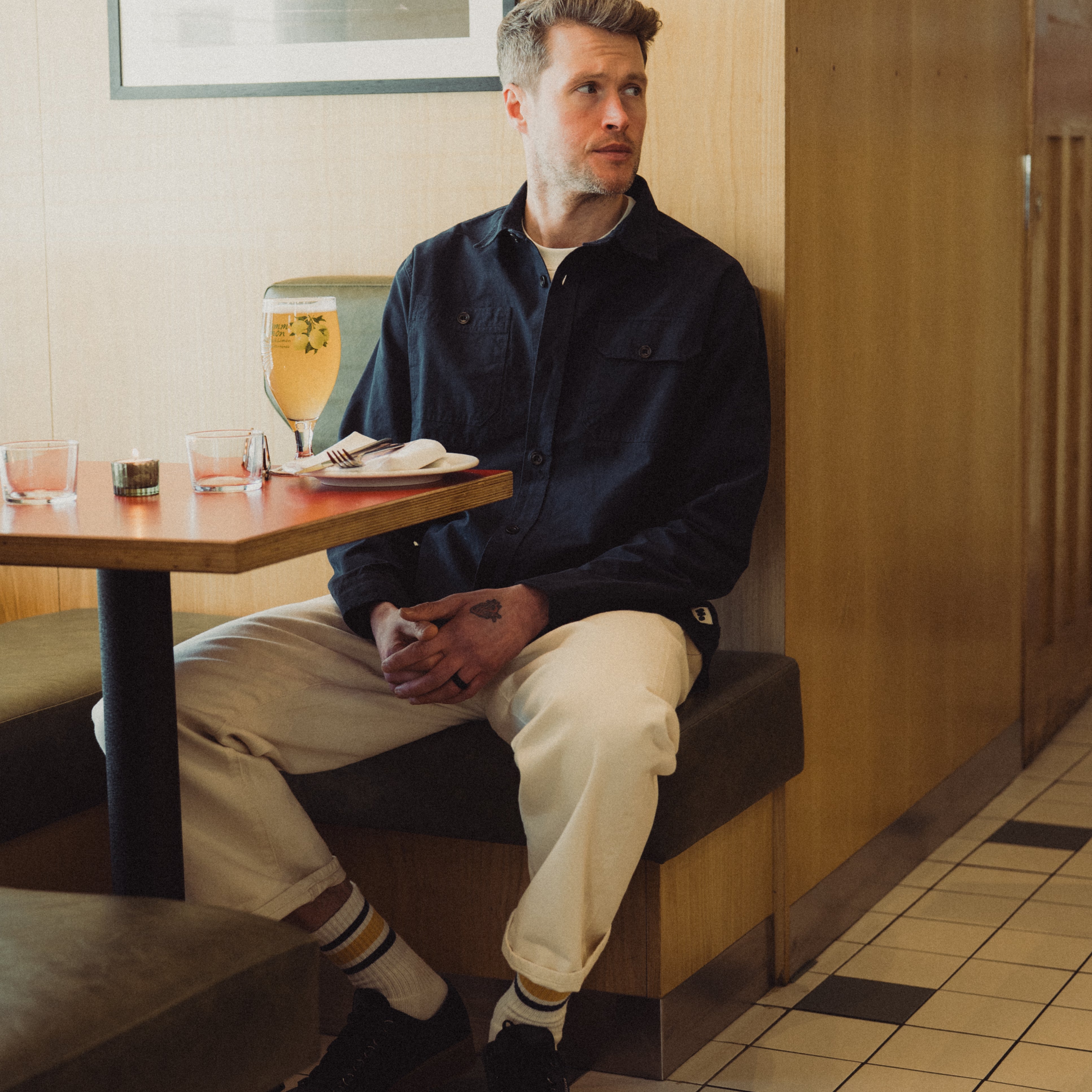 Man sitting alone in a diner booth with a drink and napkin on the table.