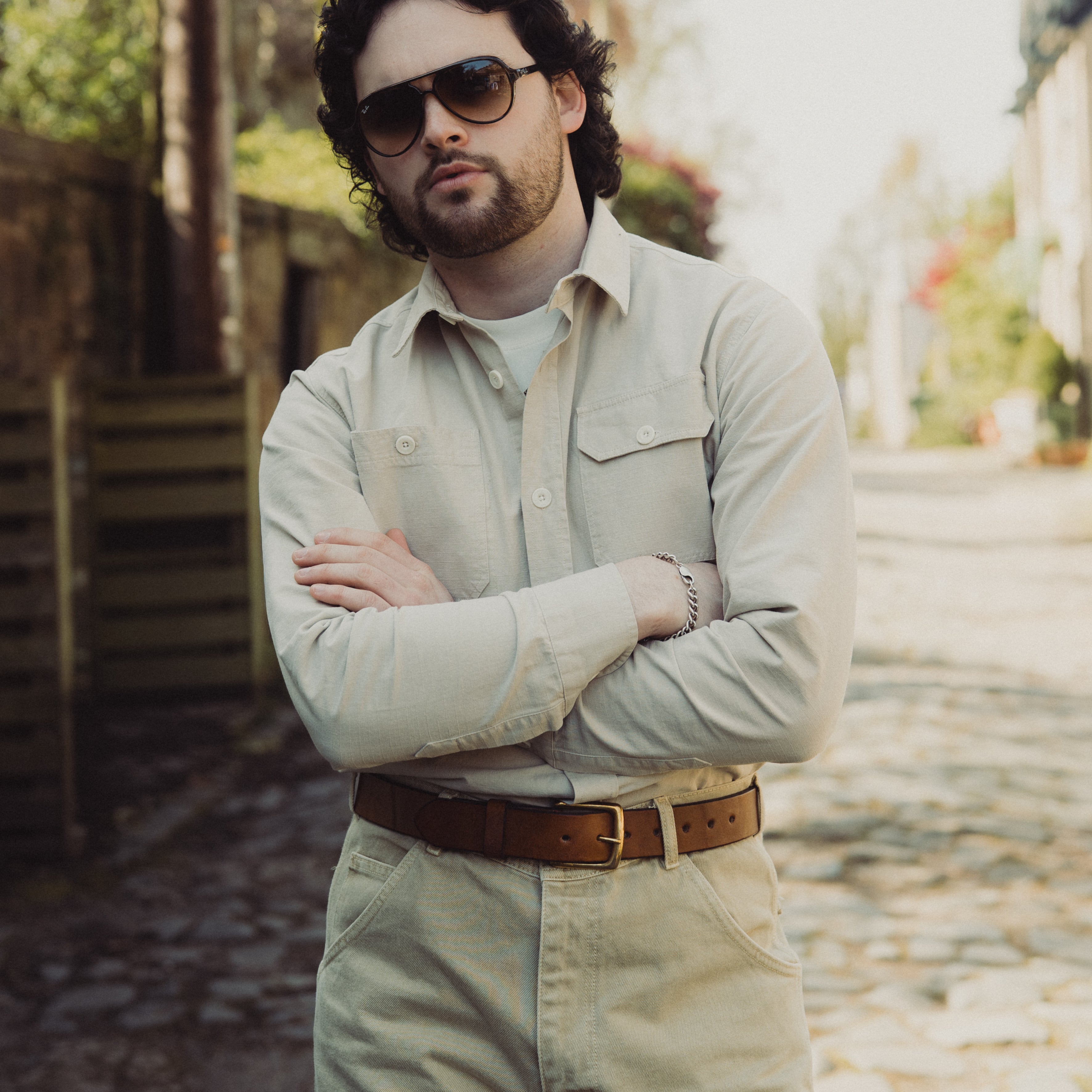 Man wearing sunglasses and a light-colored shirt with a blurred outdoor background