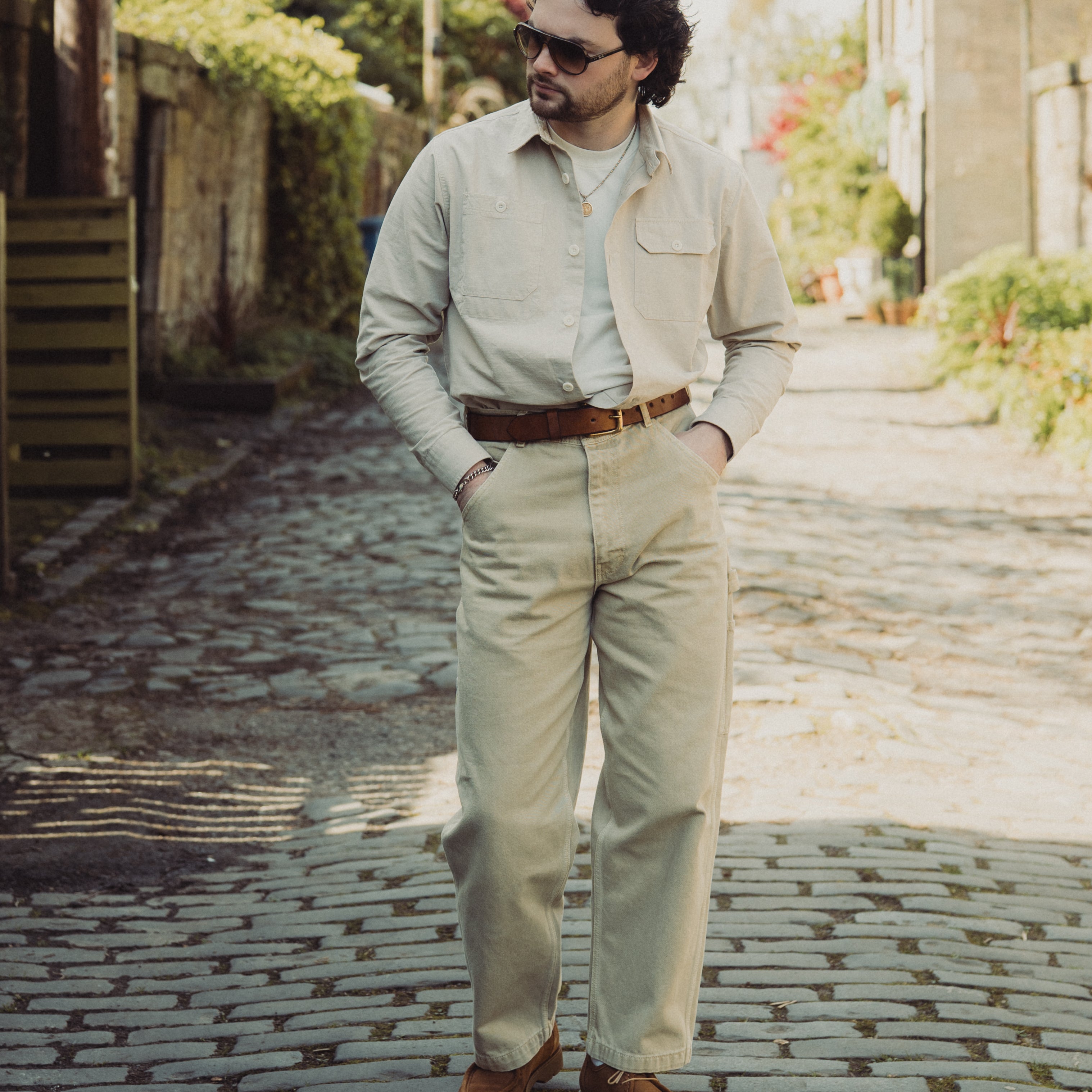 Man in beige suit and sunglasses standing on a cobblestone street.