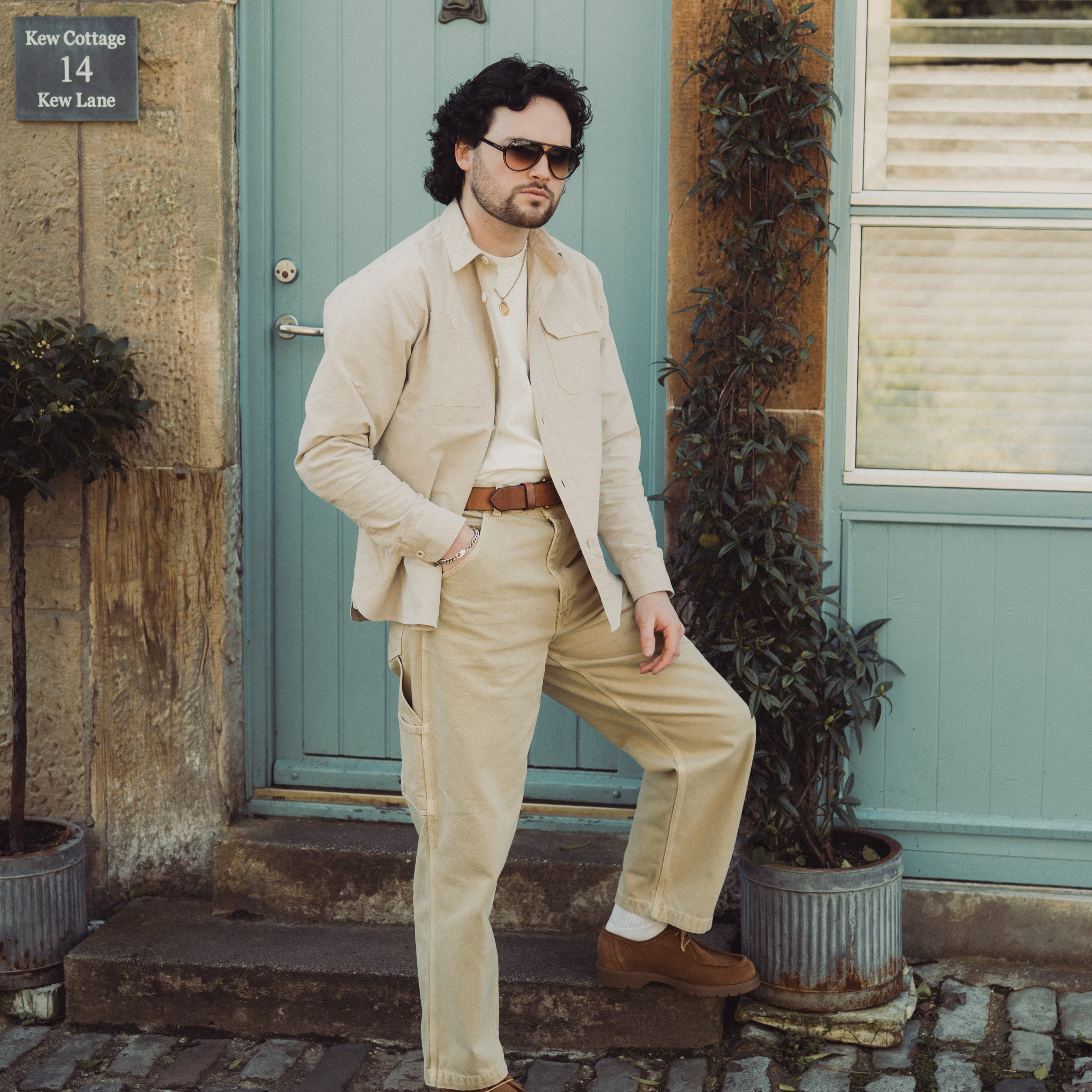 Man in beige suit standing in front of a teal door