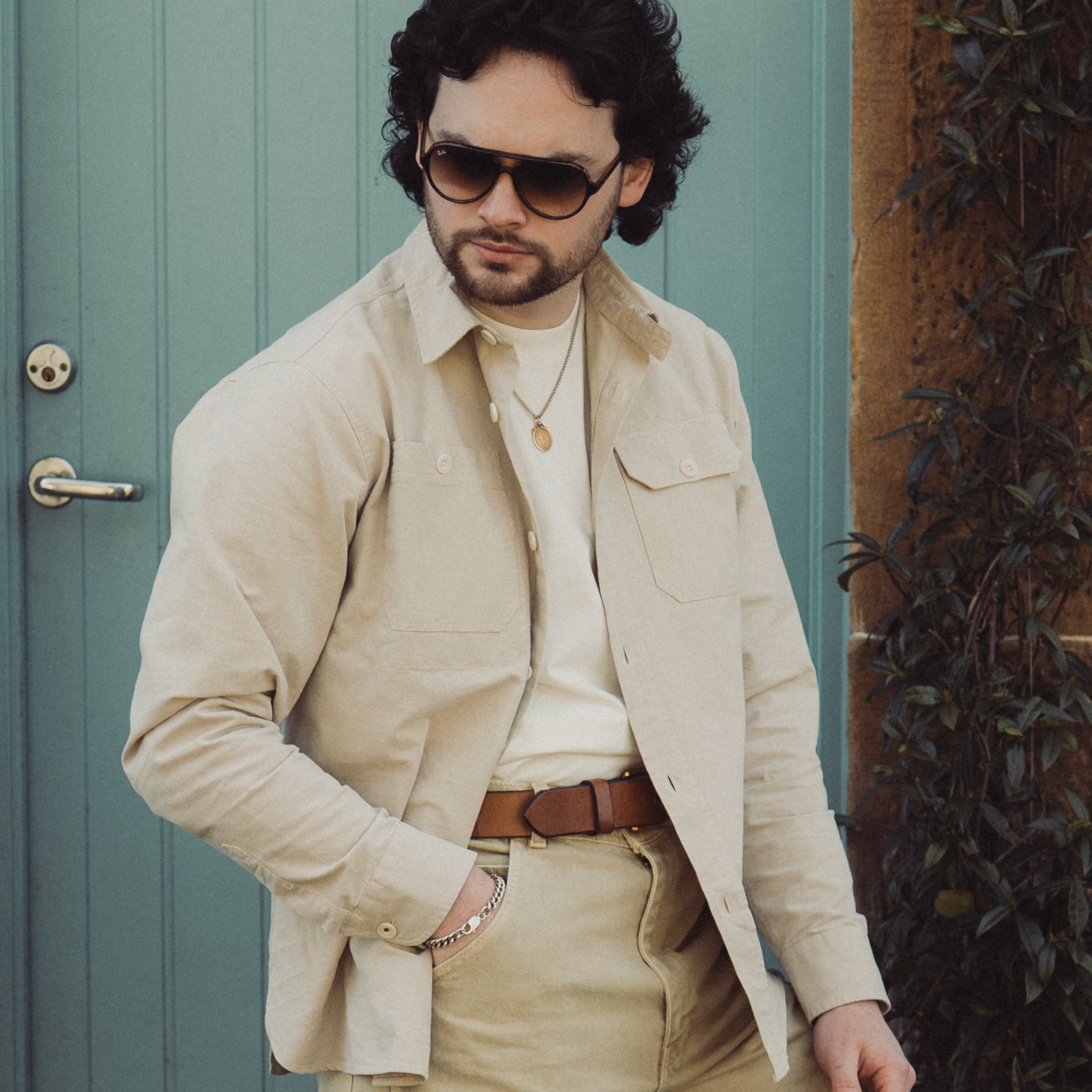 Man wearing sunglasses and a beige outfit in front of a green door.