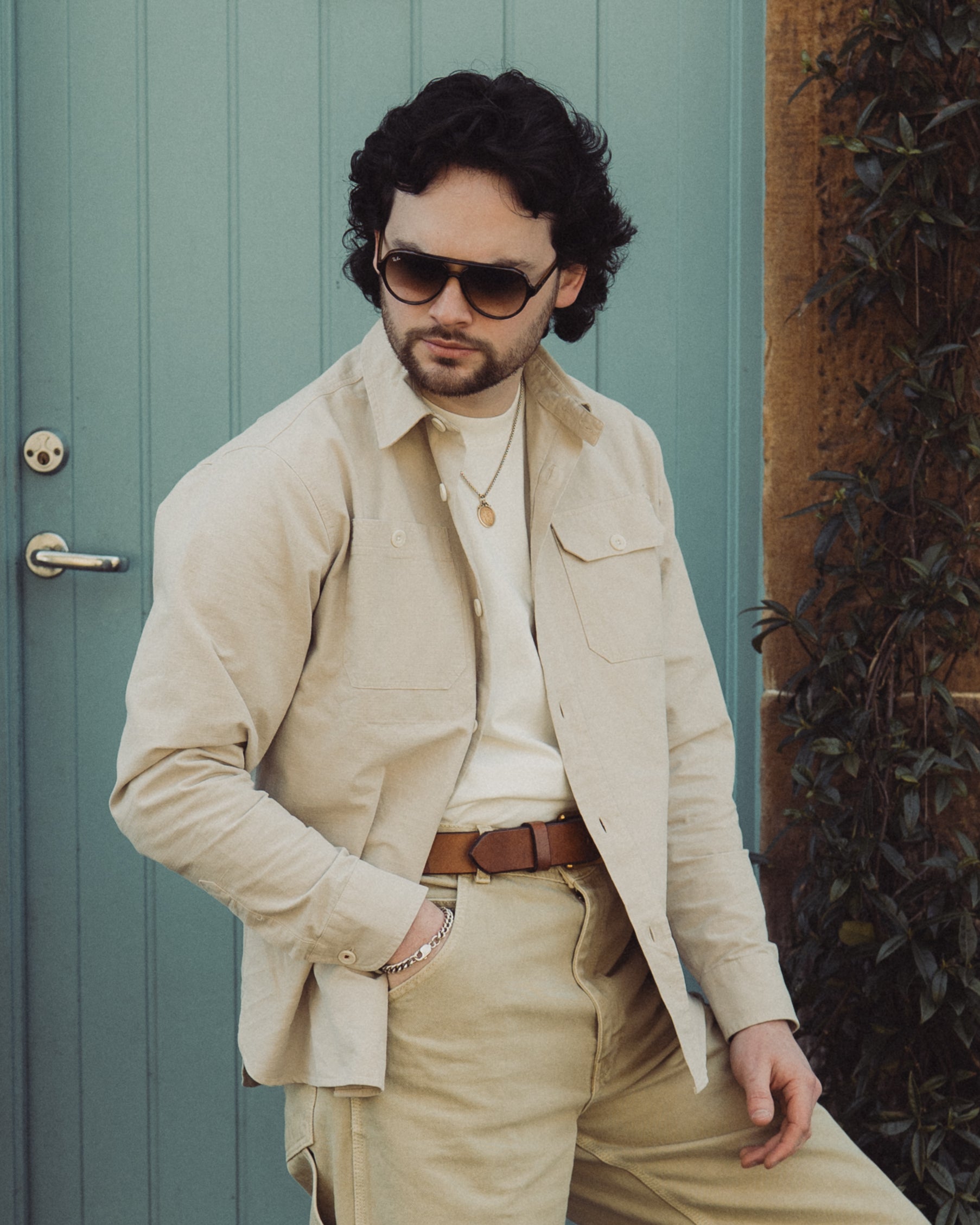 Man wearing sunglasses and a beige outfit in front of a green door.