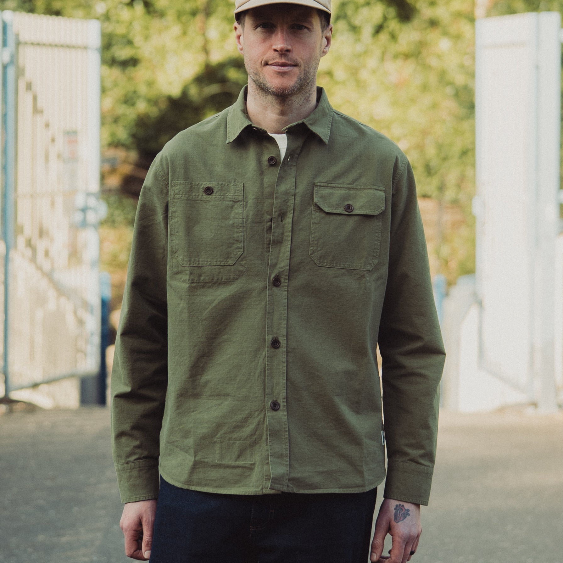 Man wearing a green jacket and beige cap standing outdoors with blurred background