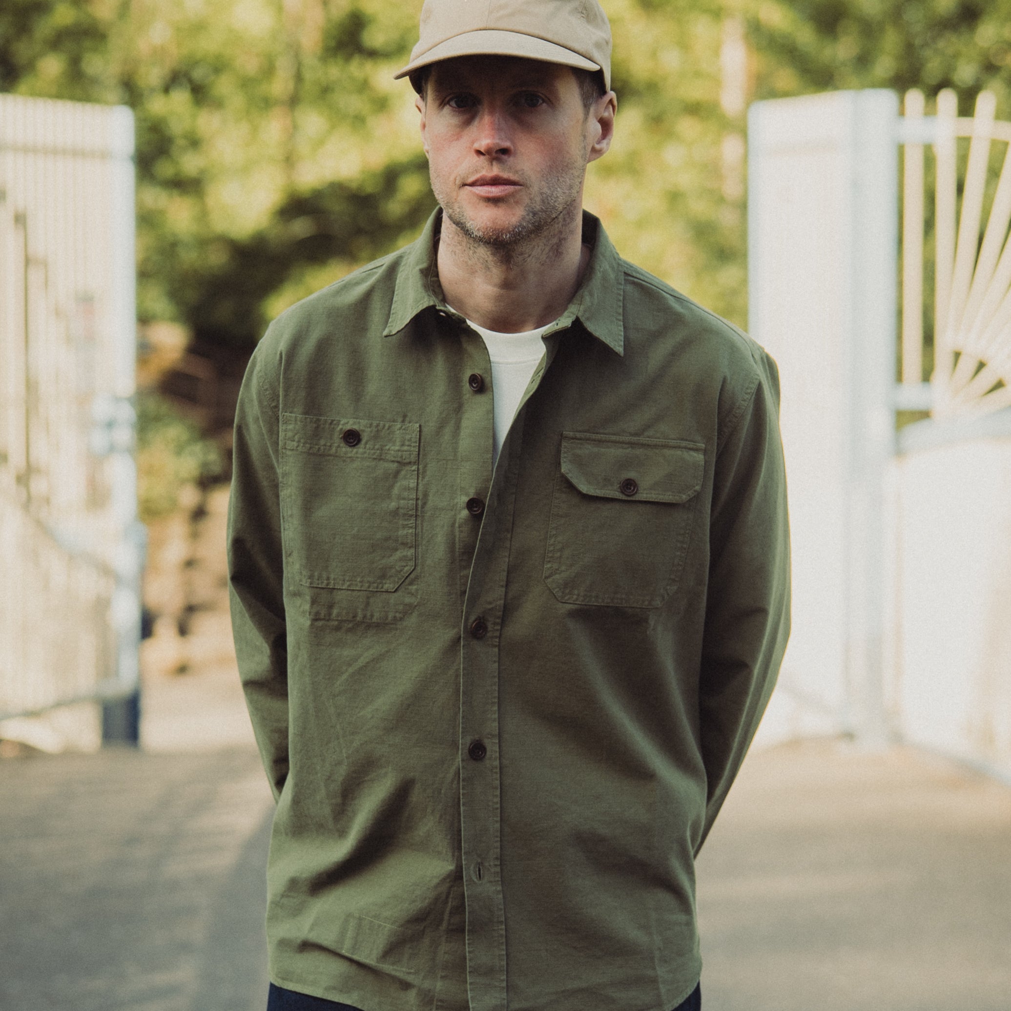Man wearing a green jacket and beige cap standing outdoors with blurred background