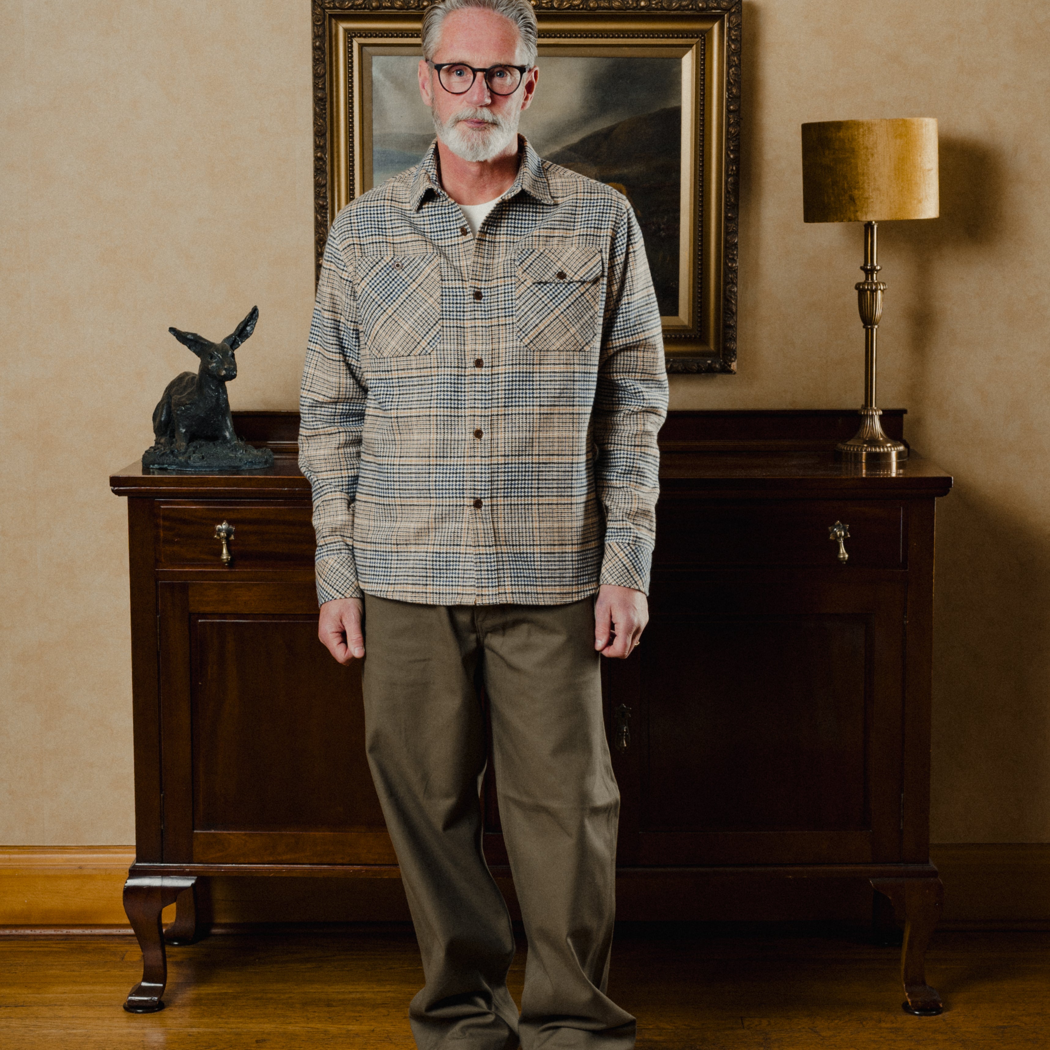 Man standing in a room with wooden furniture and a lamp.