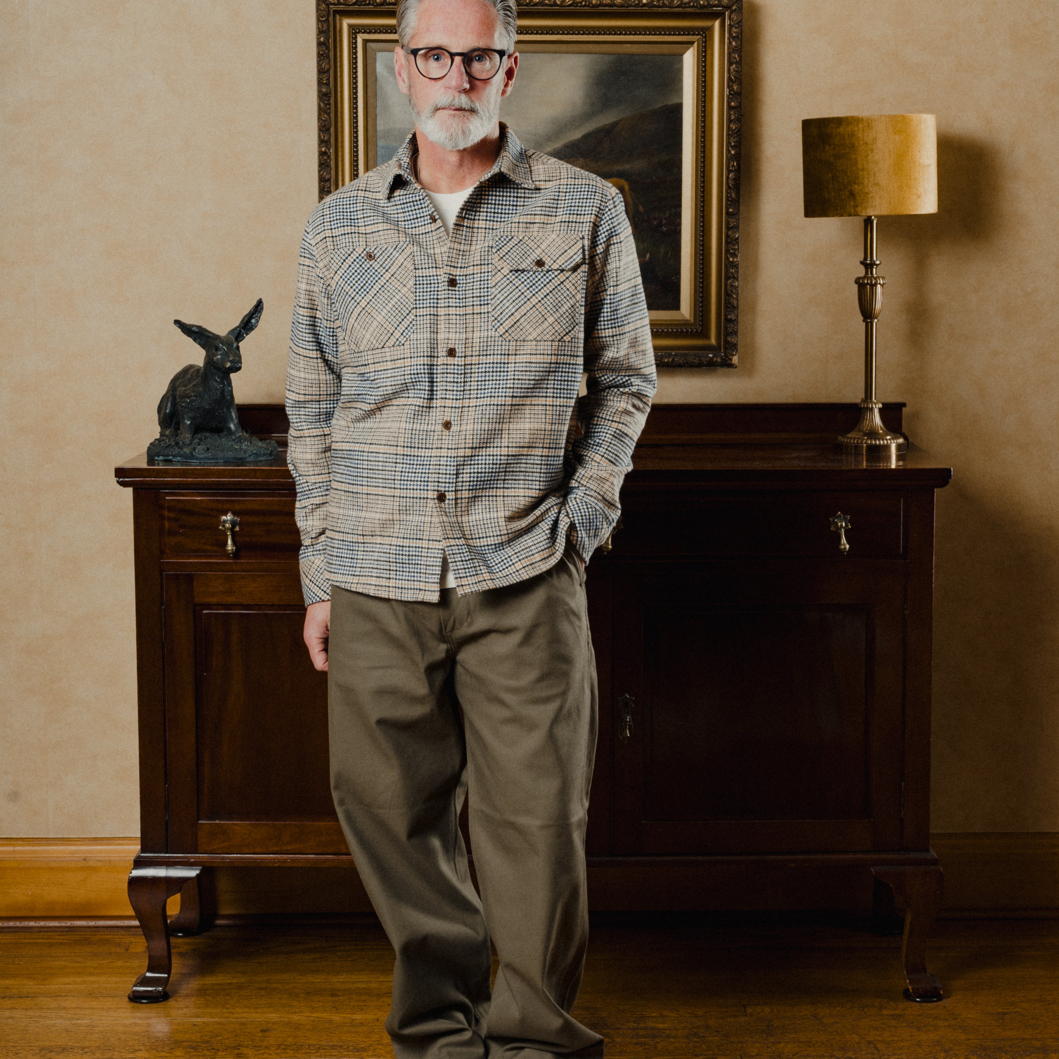 Man standing in a room with a painting and lamp in the background