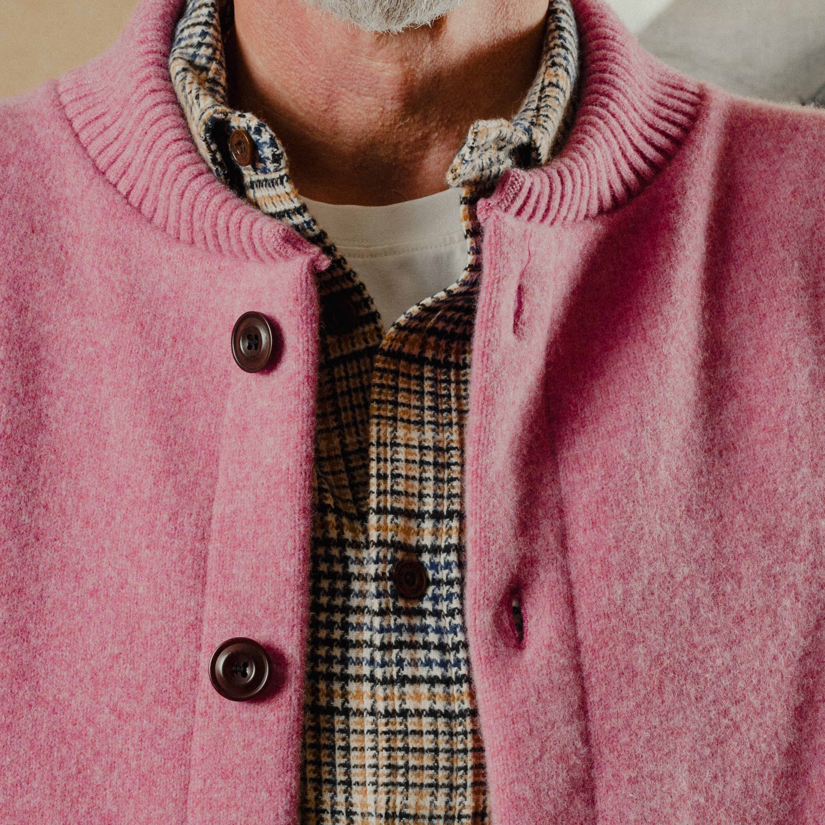 Close-up of a person wearing a pink cardigan over a plaid shirt.
