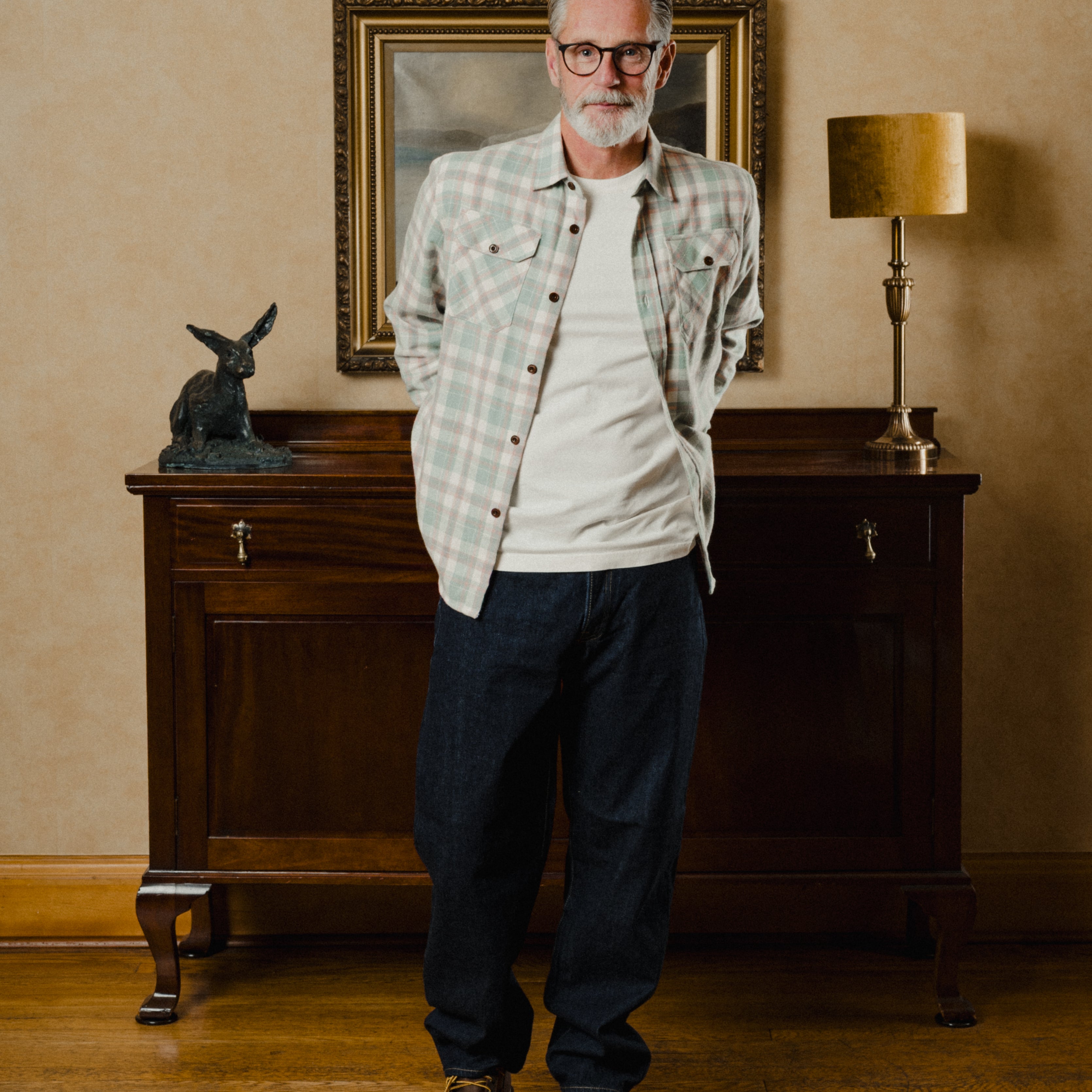 Man standing in a room with a wooden cabinet, lamp, and framed picture in the background.