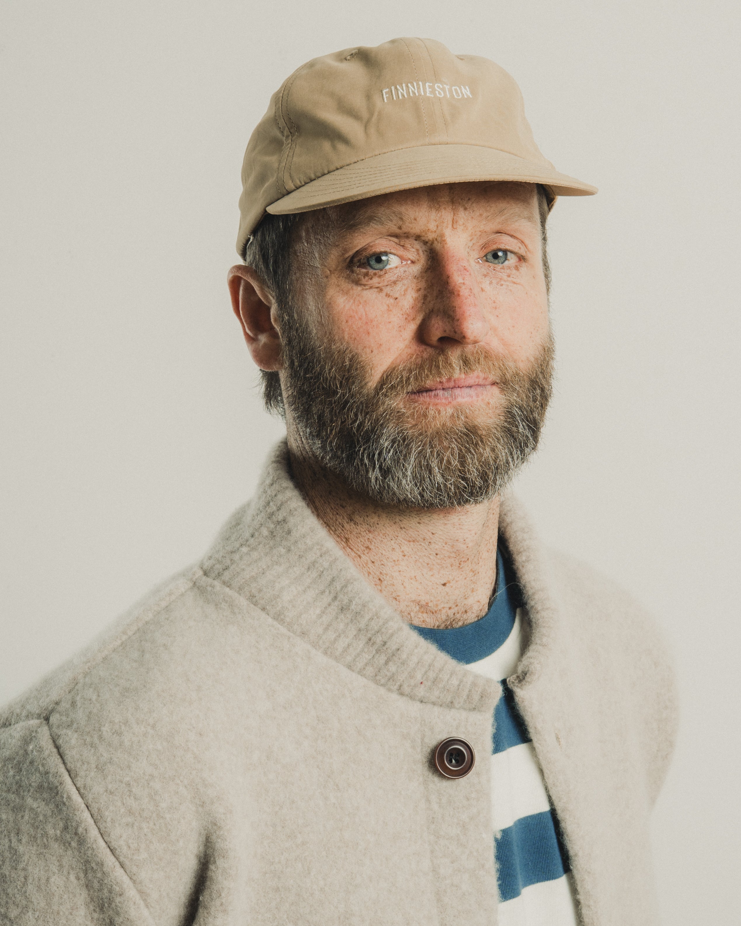 Man wearing a beige cap and light-colored jacket with a plain background