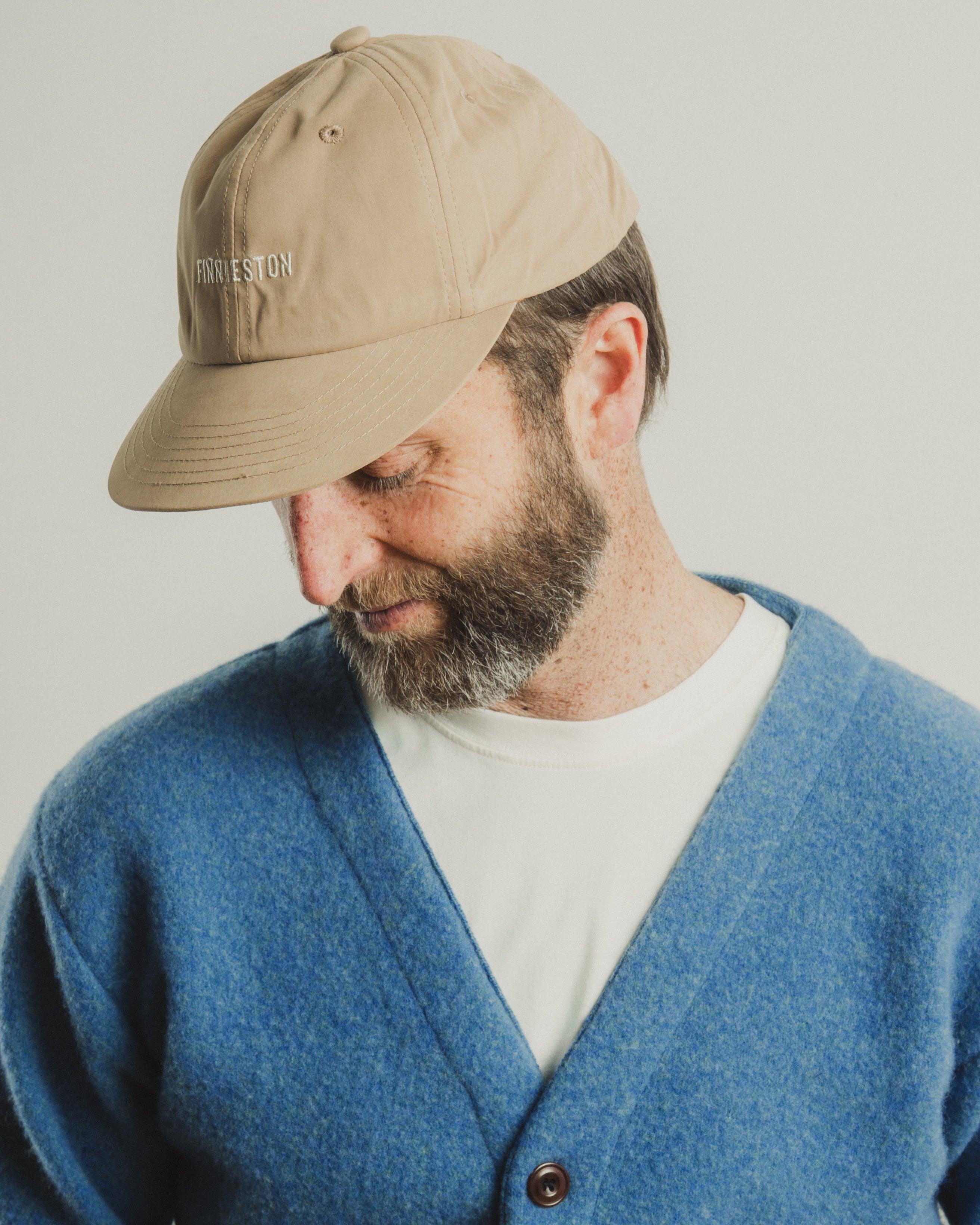 Man wearing a beige cap and blue cardigan on a plain background