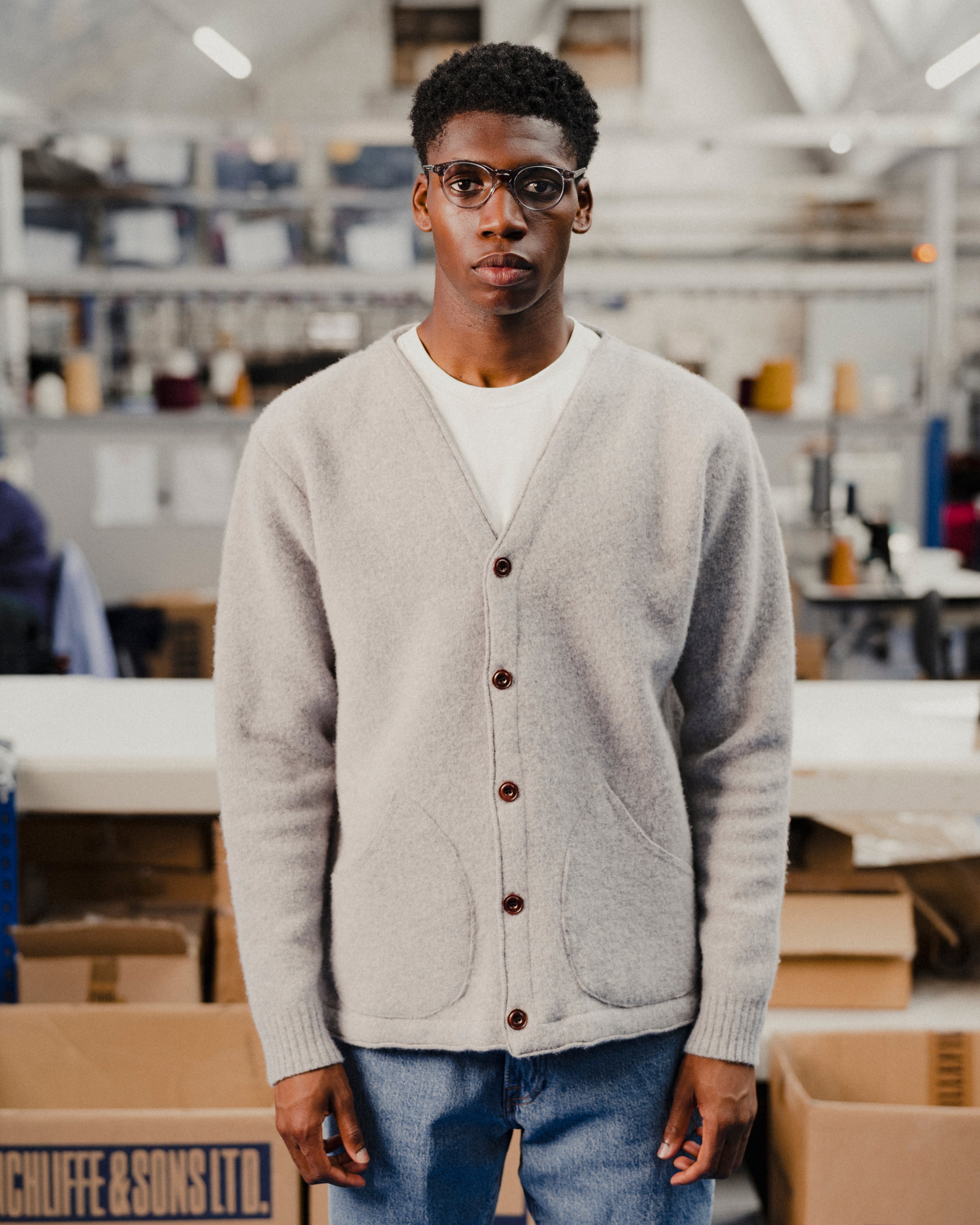 Man wearing a grey cardigan in an indoor setting with shelves and boxes in the background