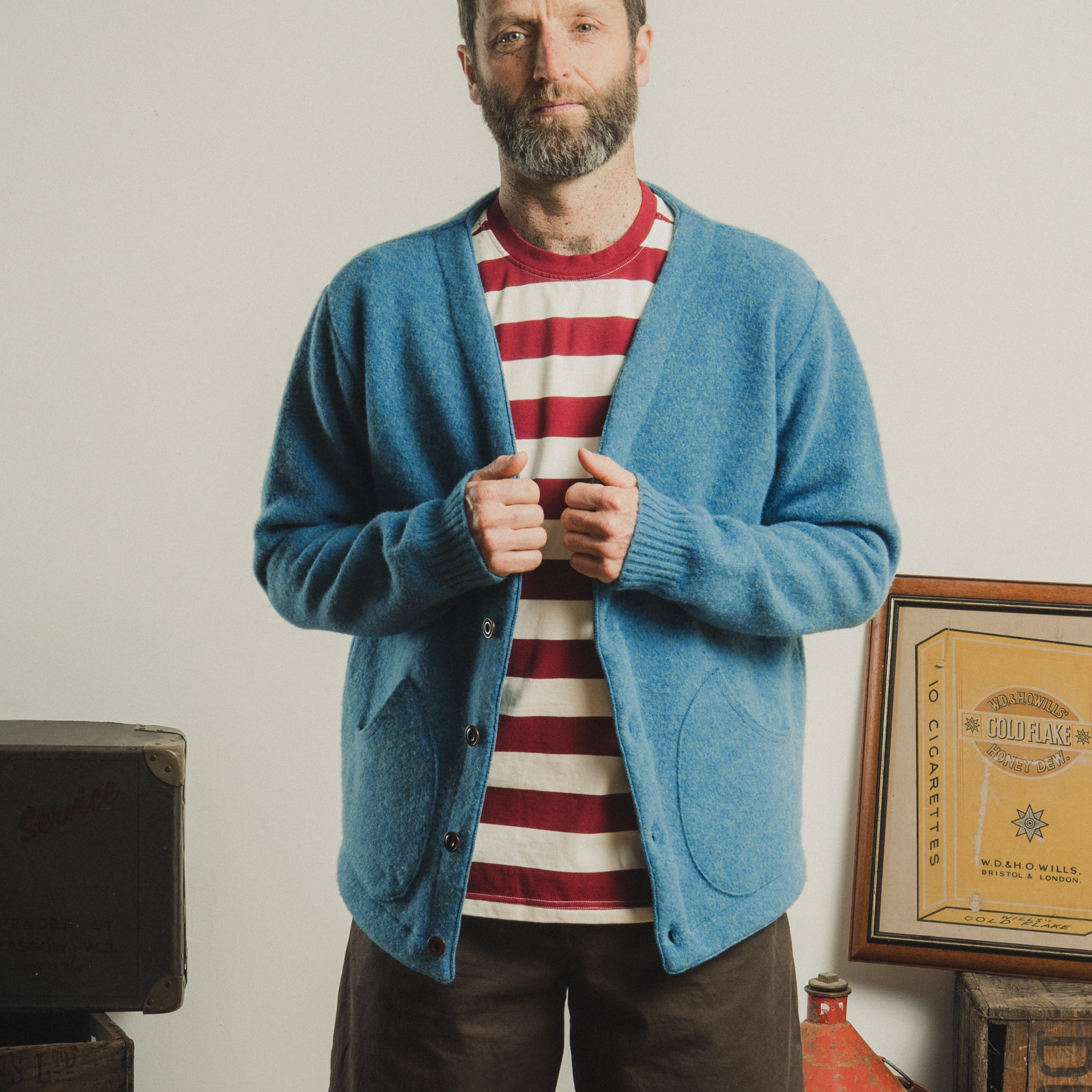 Man wearing a blue cardigan over a red and white striped shirt, standing in a room with vintage decor.
