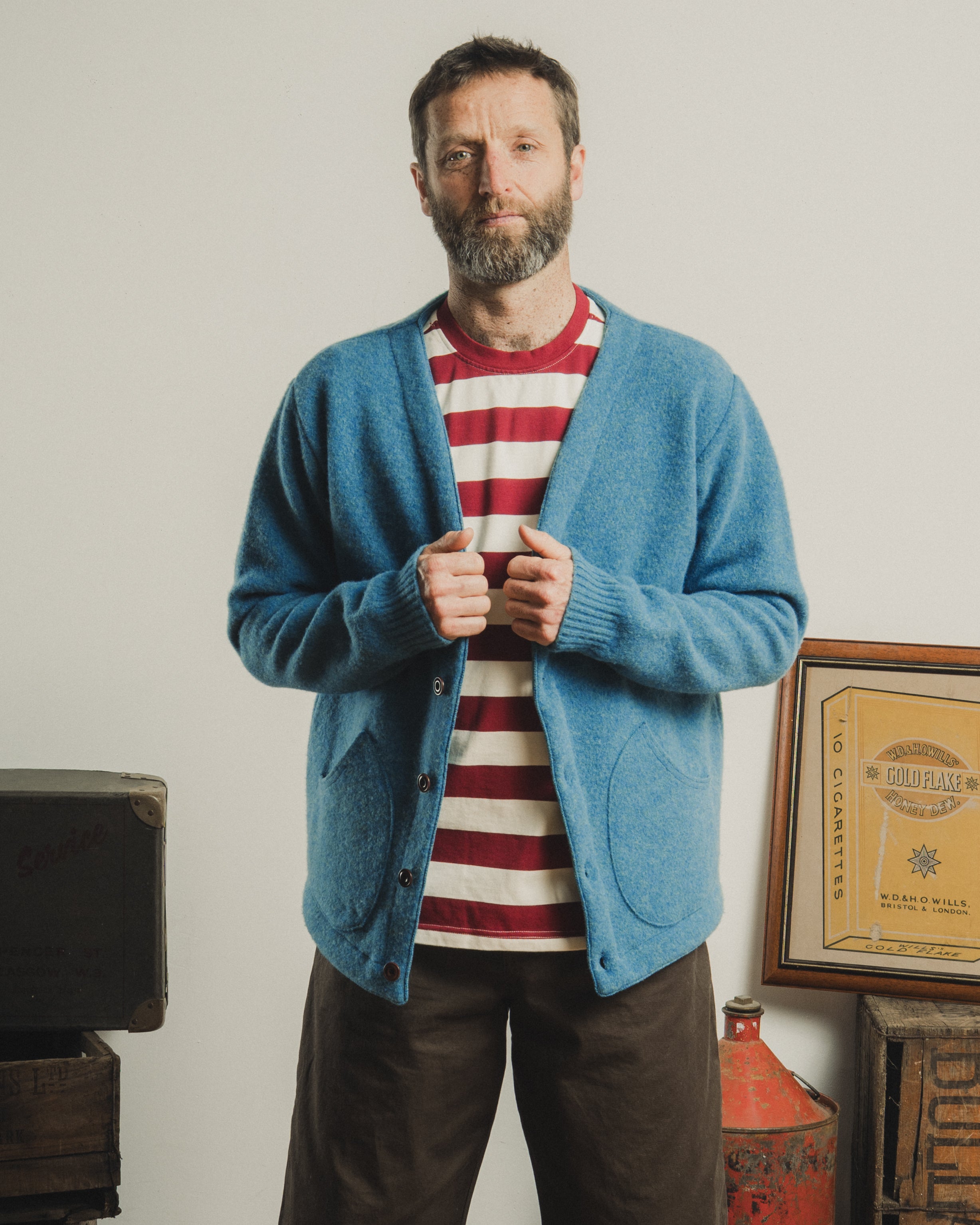 Man wearing a blue cardigan over a red and white striped shirt, standing in a room with vintage decor.