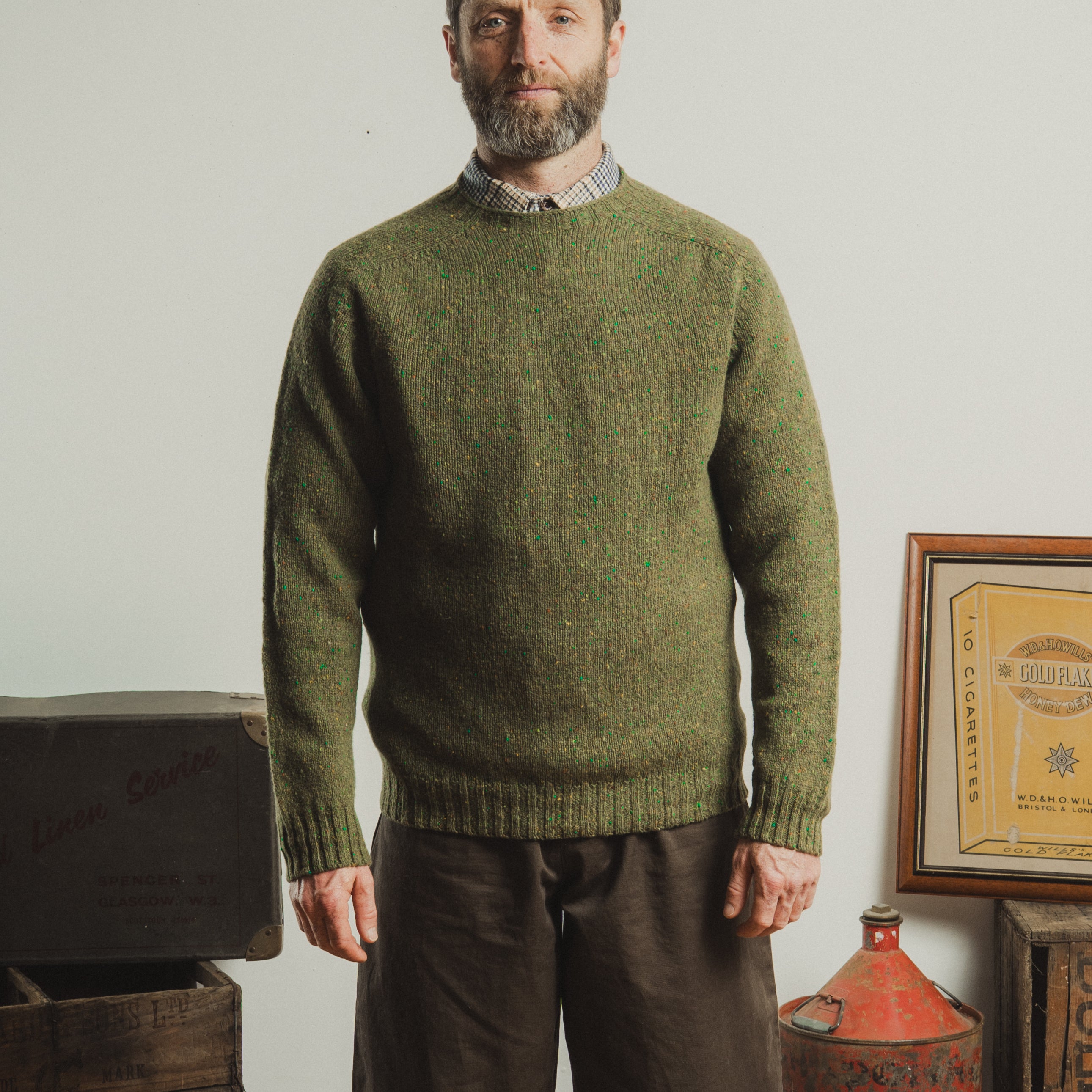 Man wearing a green knitted sweater standing in a room with vintage items.