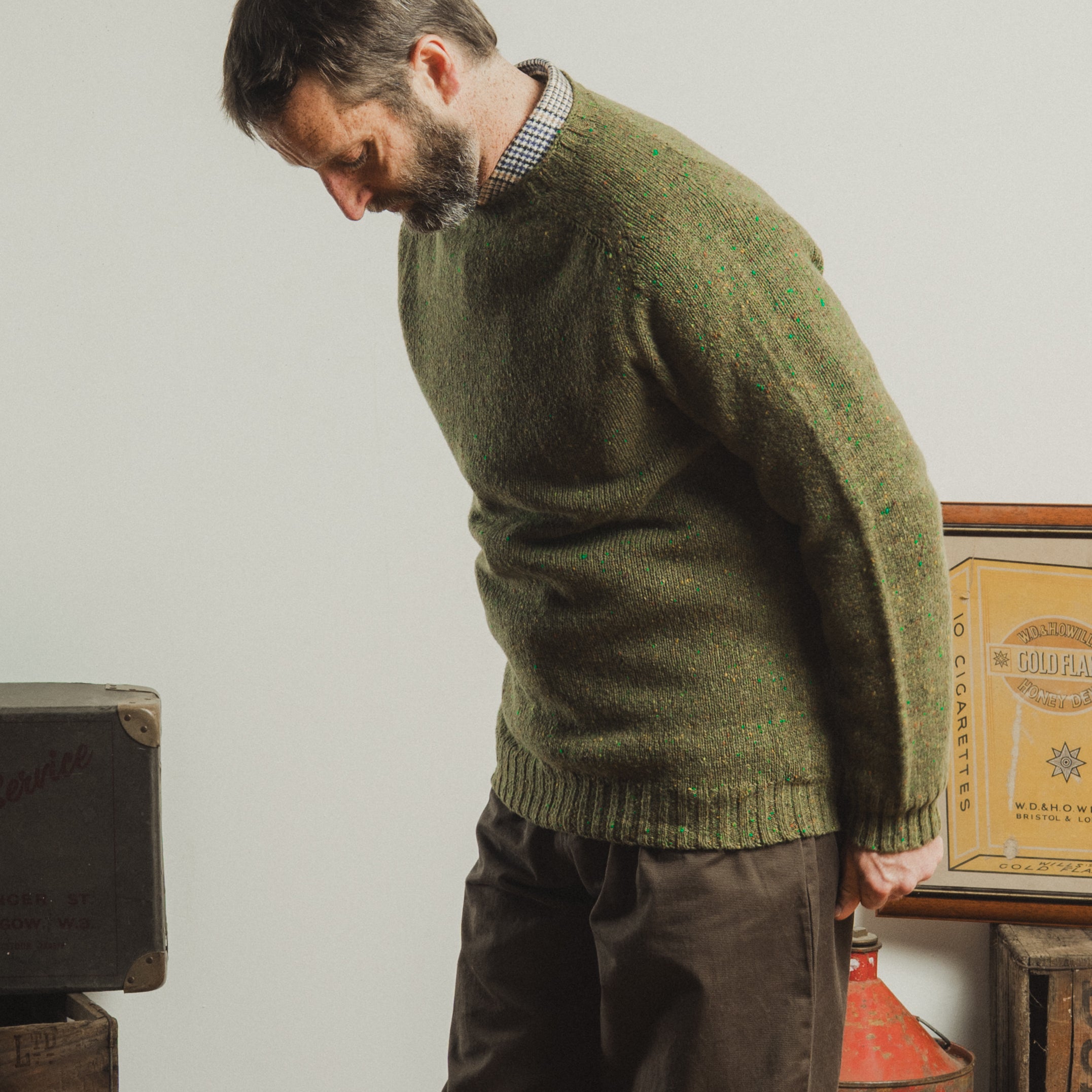 Man wearing a green knitted sweater in a room with vintage boxes.