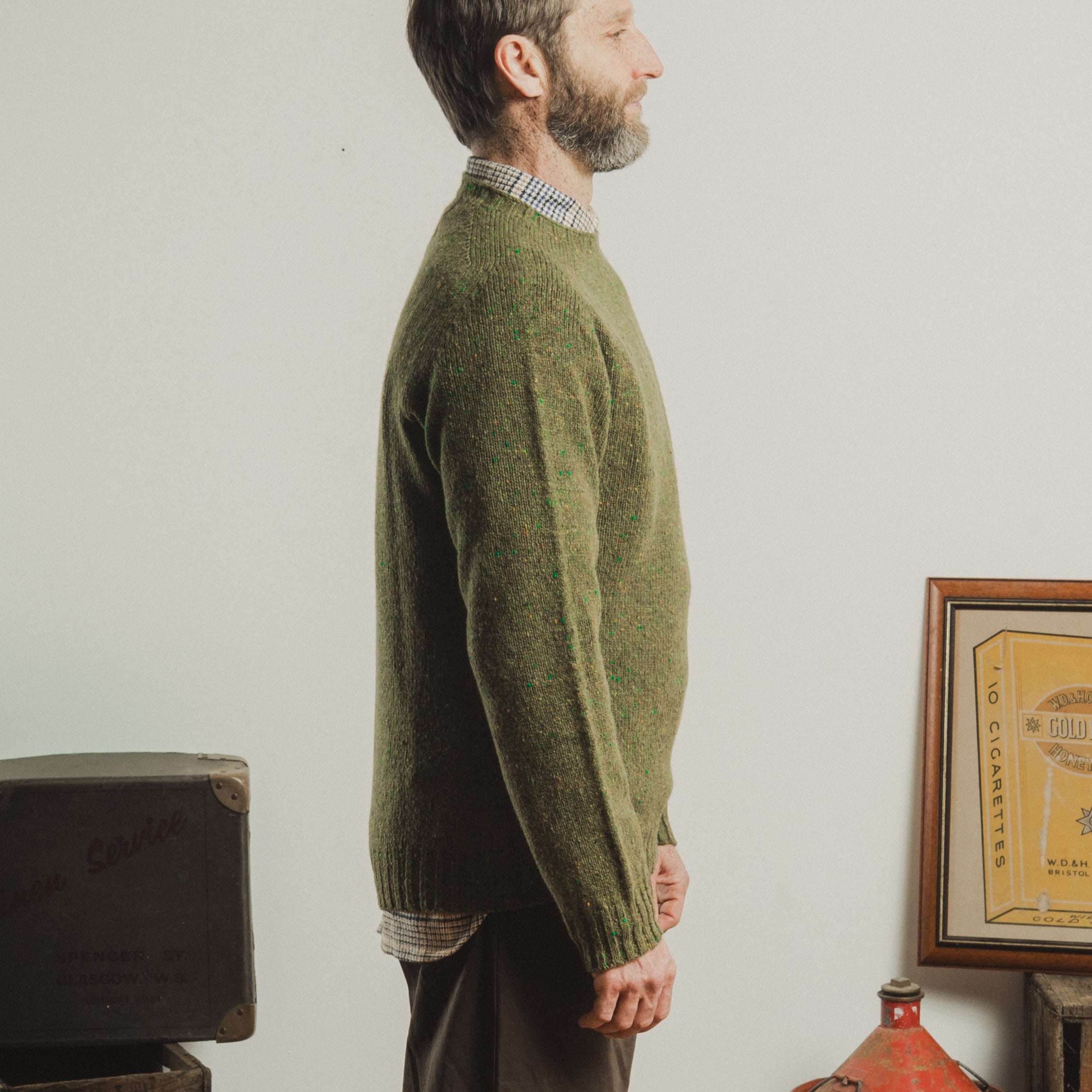 Man wearing a green sweater standing in a room with a white wall and vintage items.