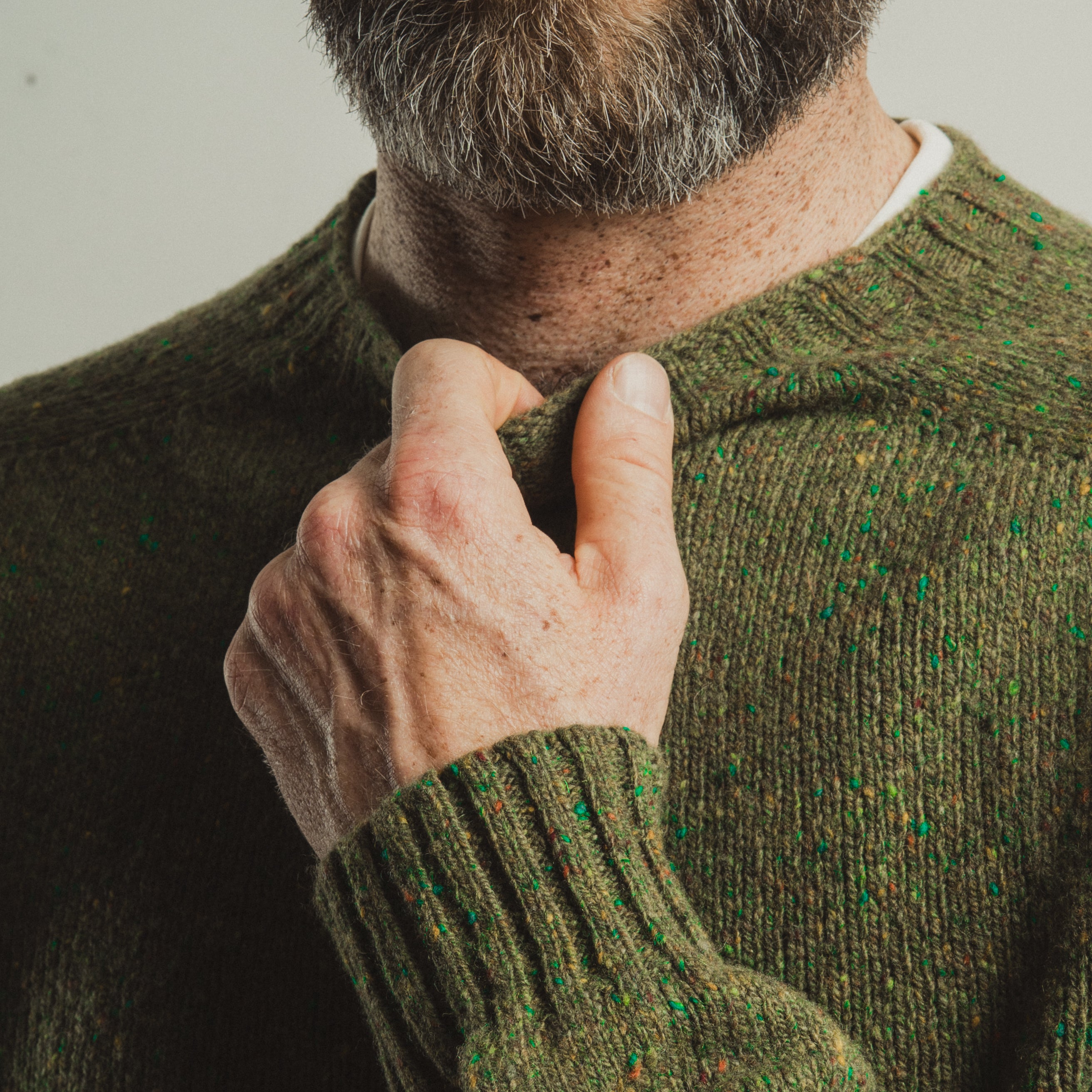 Man wearing a green sweater adjusting his collar against a neutral background