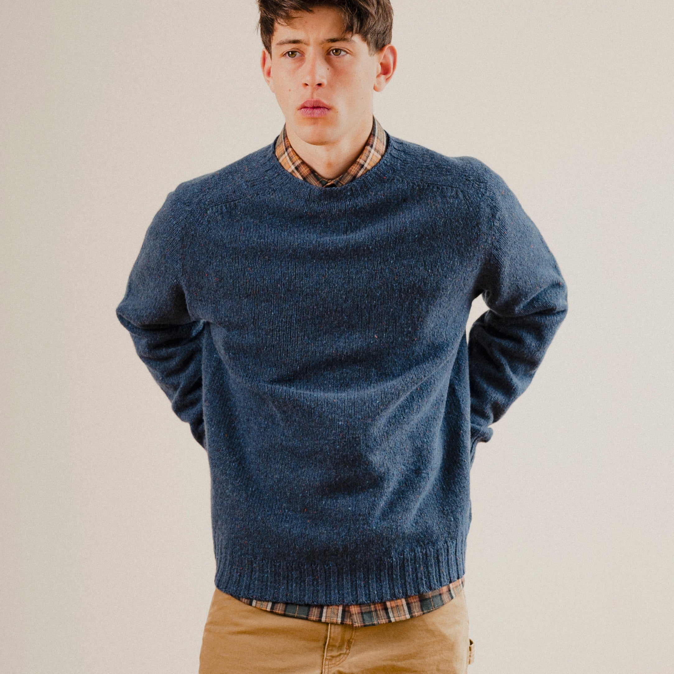 Man wearing a navy blue wool sweater knit crewneck with a check shirt