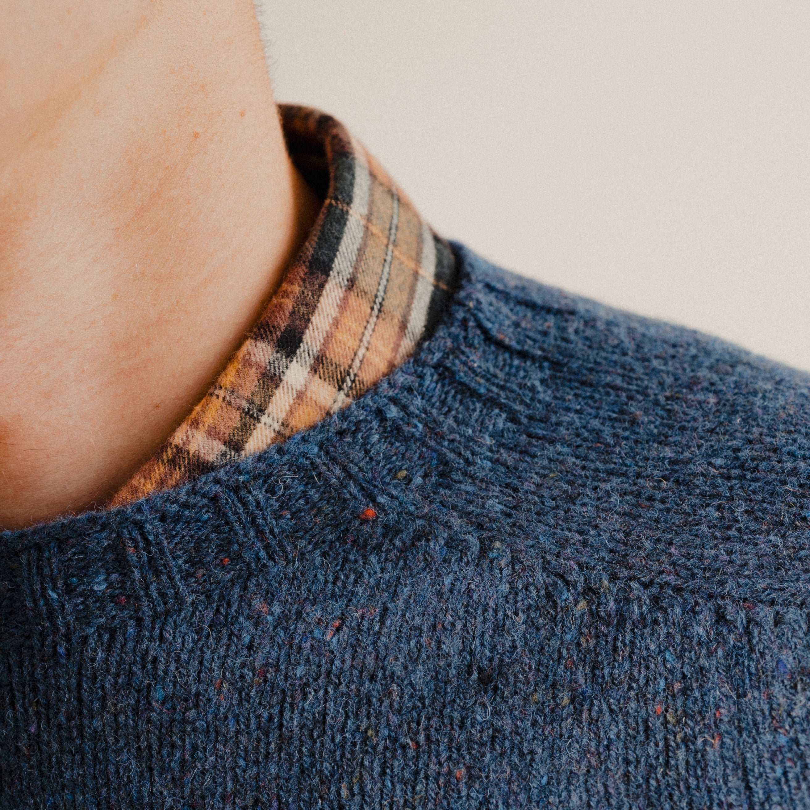 Close up on the neckline of a navy blue wool sweater knit crewneck with a check shirt underneath