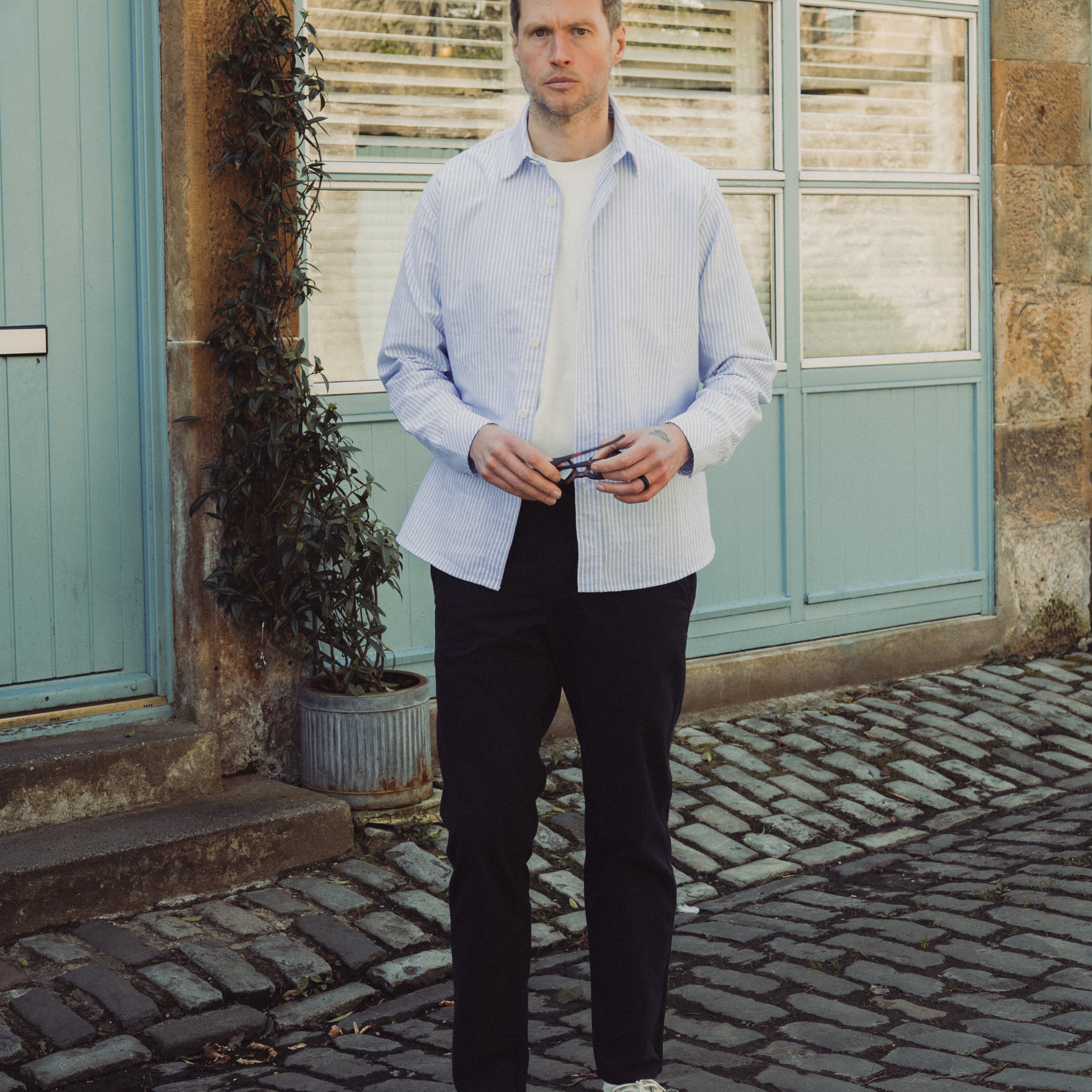 Man standing on a cobblestone street in front of a building with a light blue door.