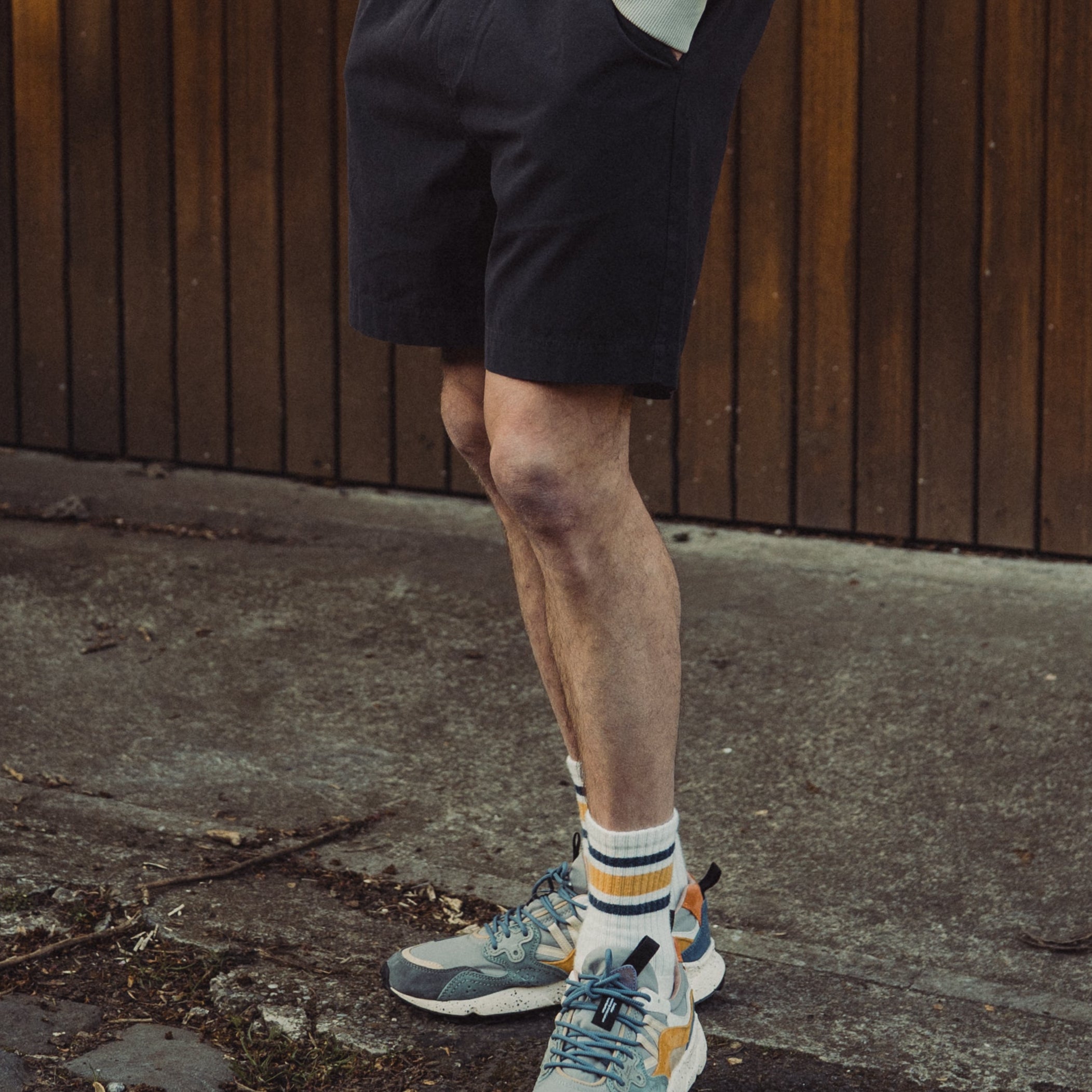 Man wearing a light gray sweatshirt and black shorts standing against a wooden wall.