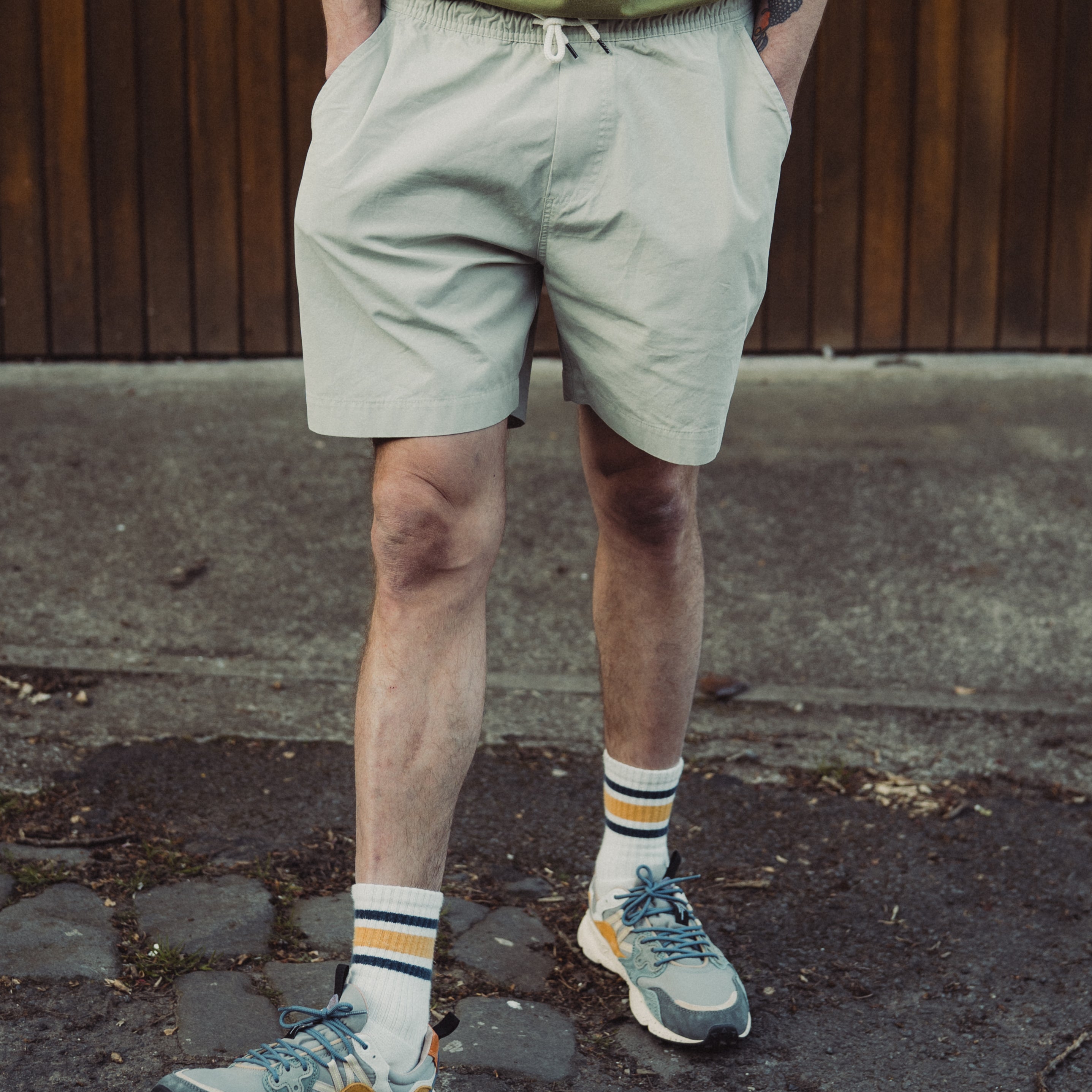 Person wearing light-colored shorts and colorful sneakers on a pavement.