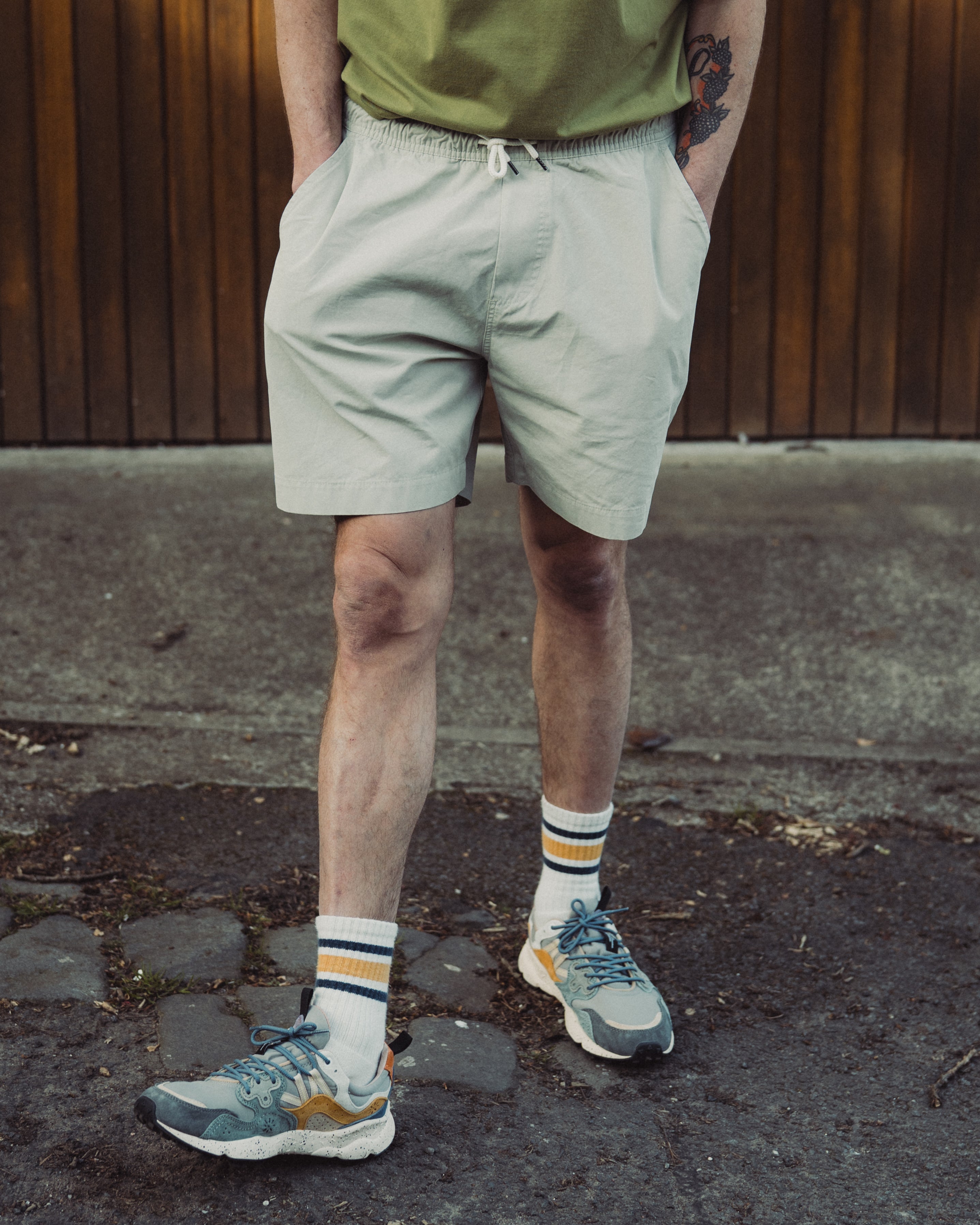 Person wearing light-colored shorts and colorful sneakers on a pavement.