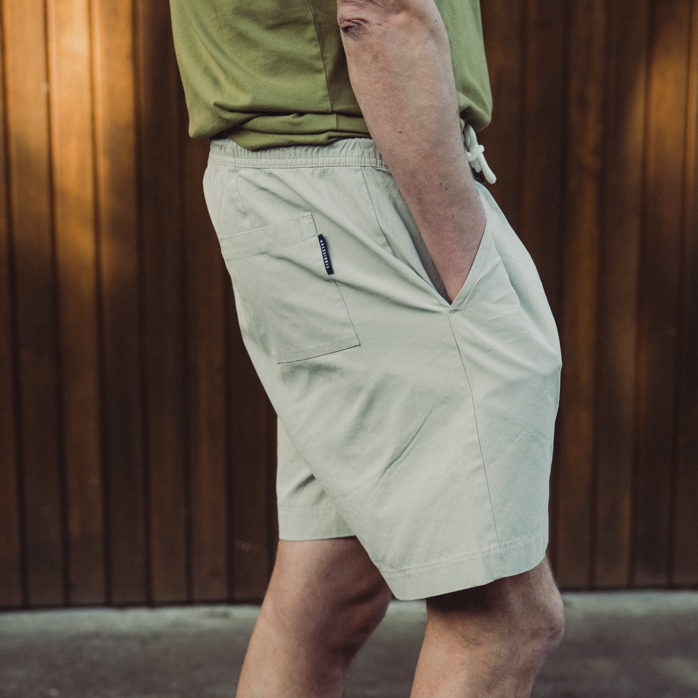 Person wearing light-colored shorts and a green shirt against a wooden wall.