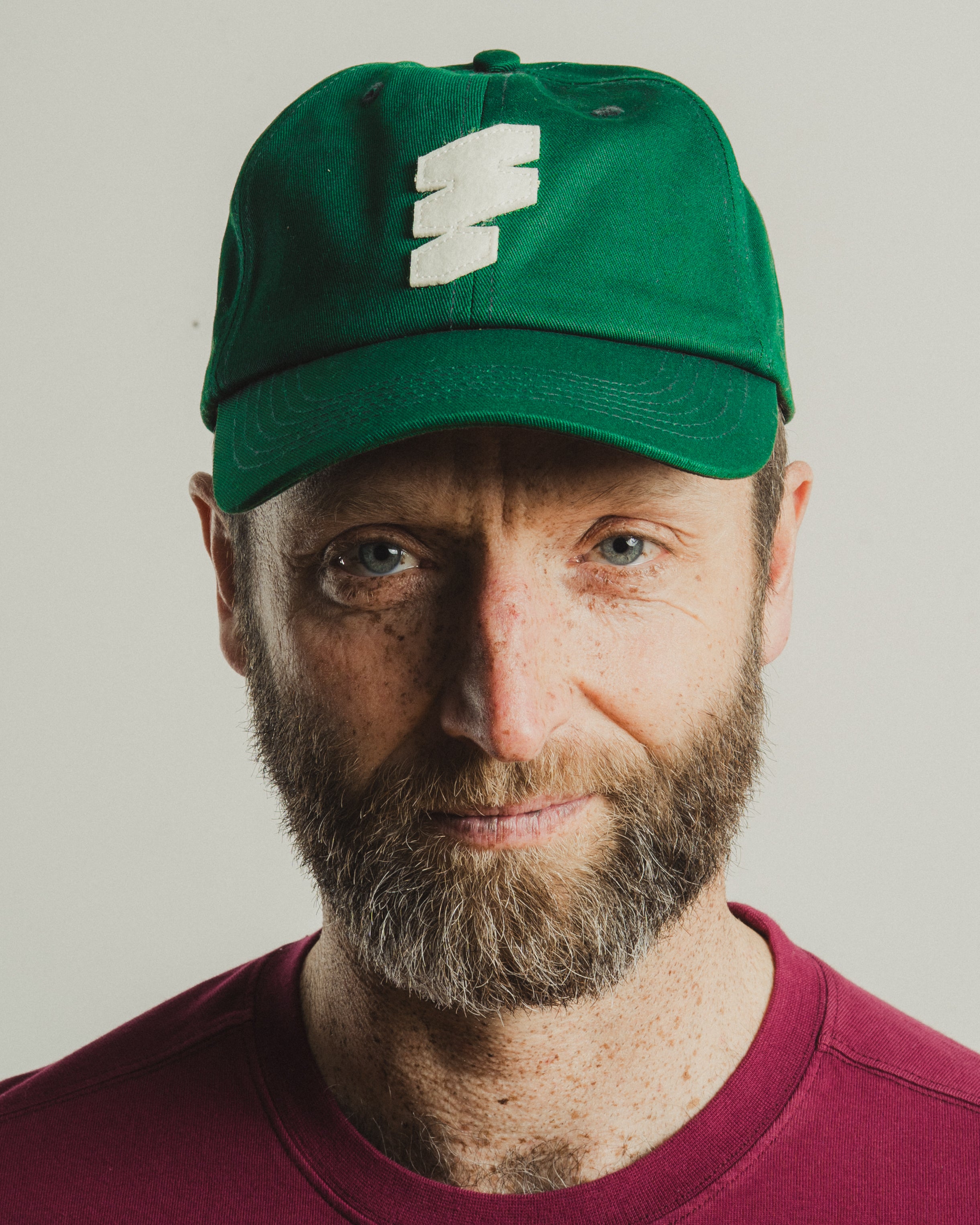 Man wearing a green cap with a logo on a plain background