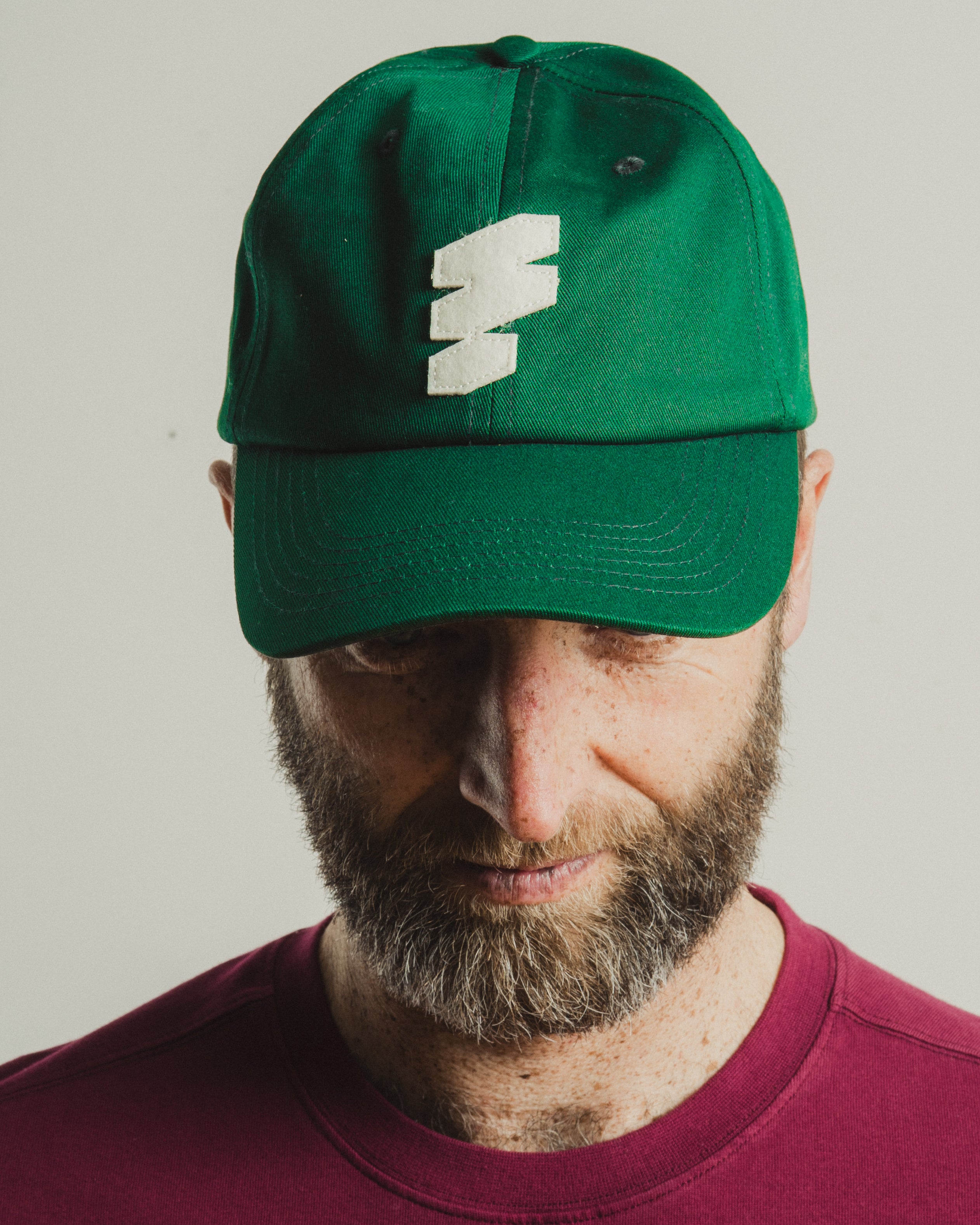 Person wearing a green cap with a logo on a plain background