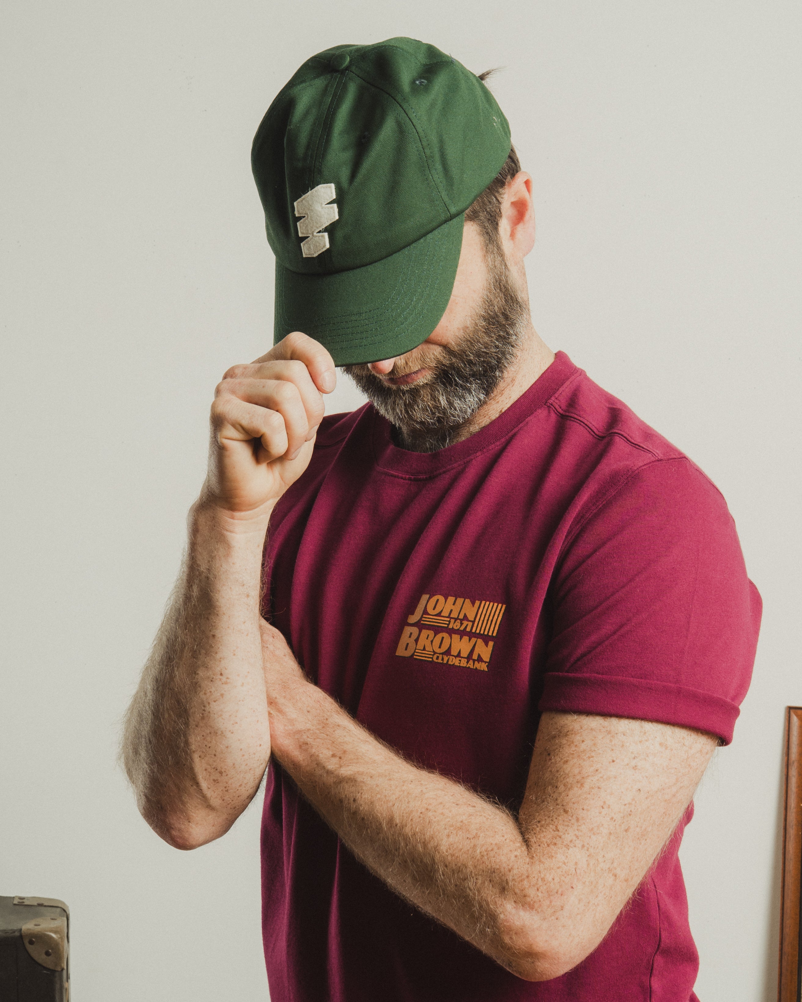 Man wearing a green cap and maroon t-shirt with text, against a plain background