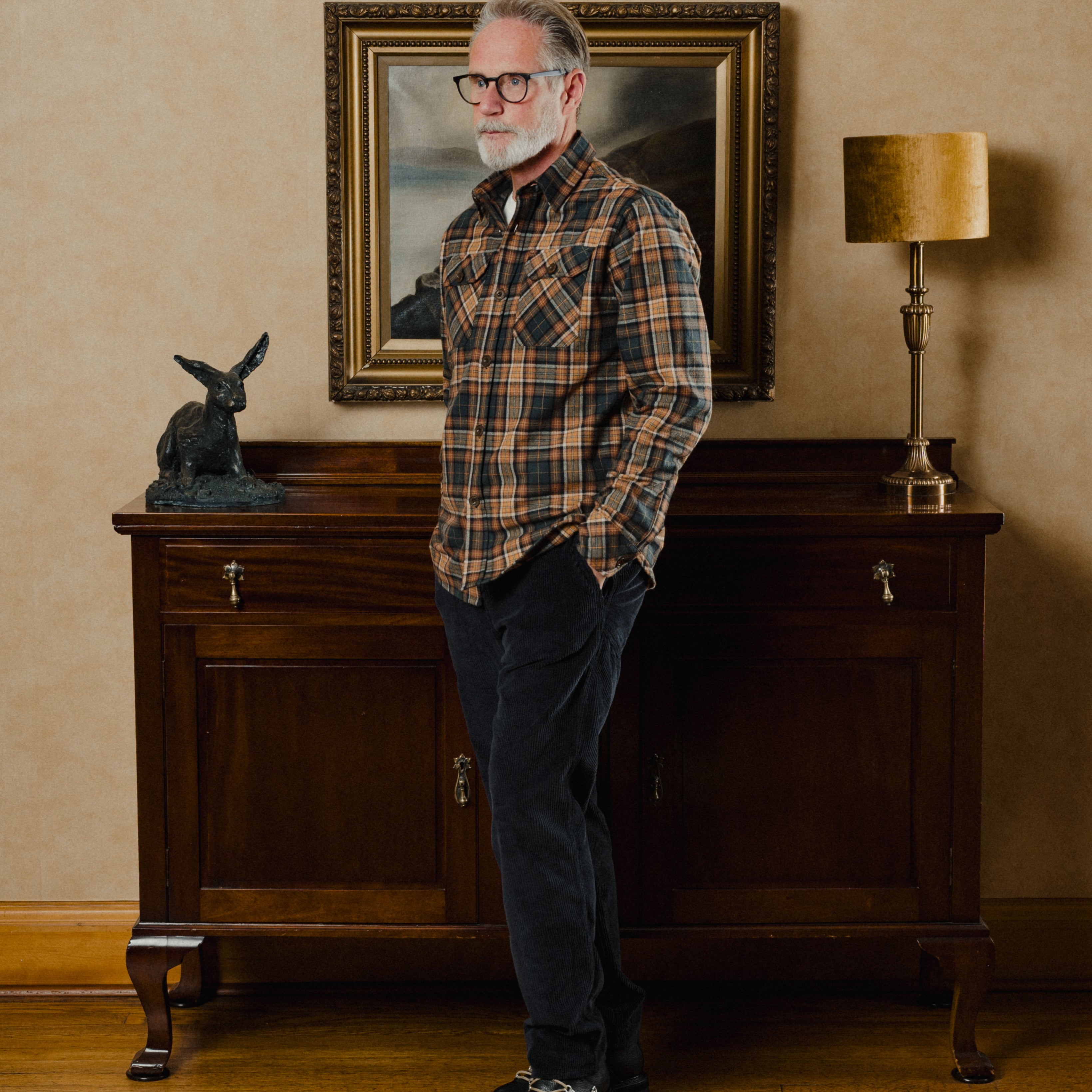 Man in plaid shirt standing in a room with wooden furniture and decorative items.