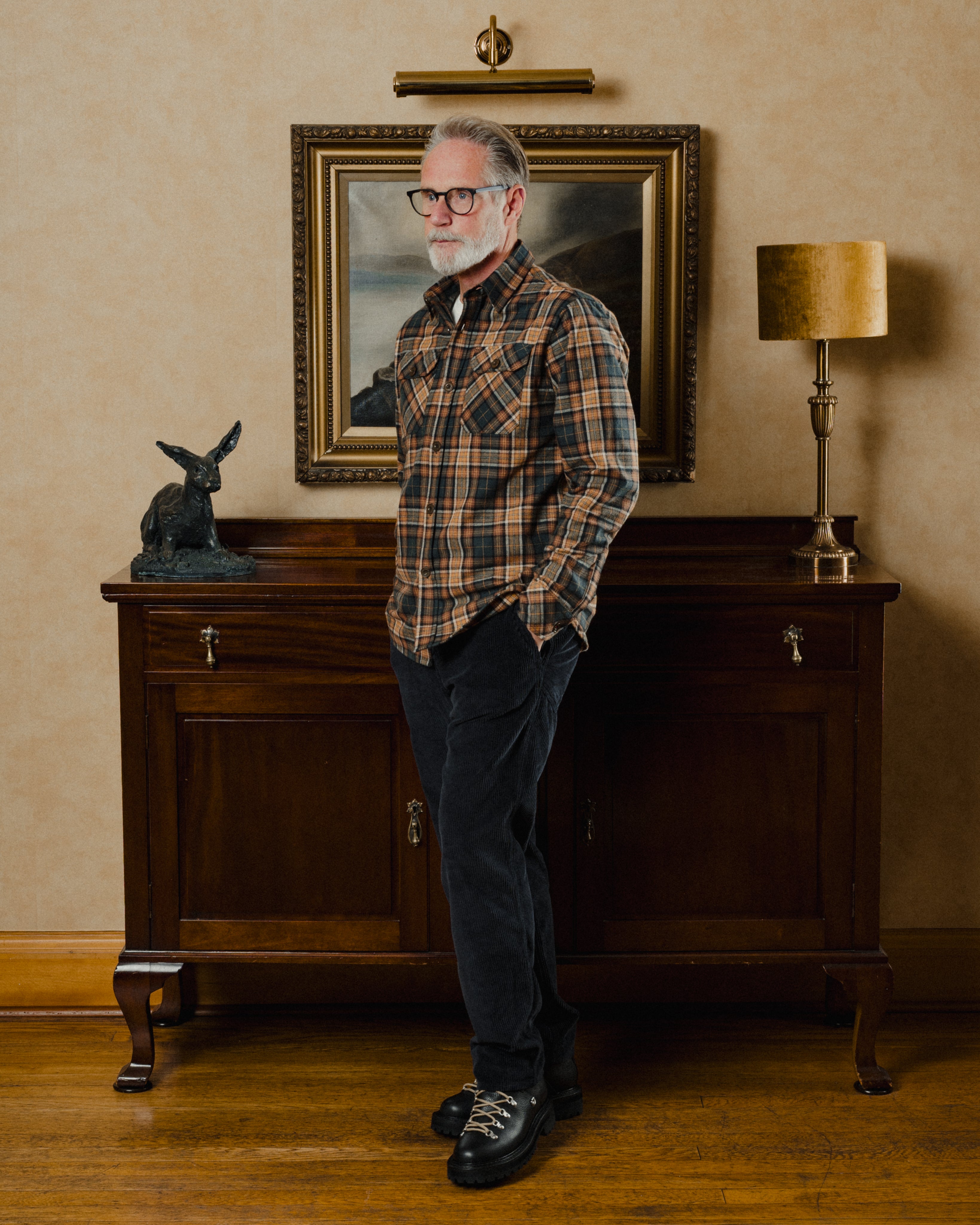Man in plaid shirt standing in a room with wooden furniture and decorative items.