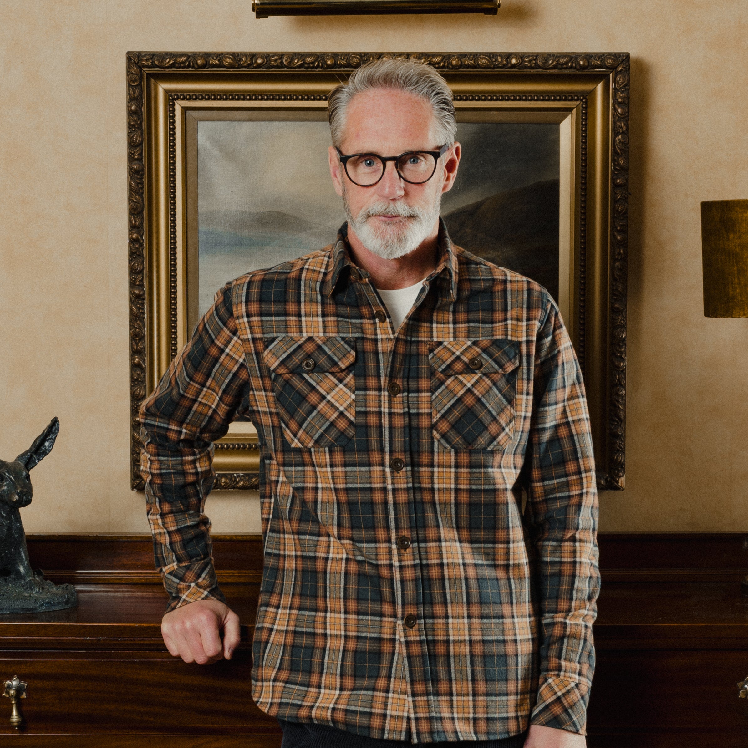 Man wearing a plaid shirt standing in front of a painting on a wall.