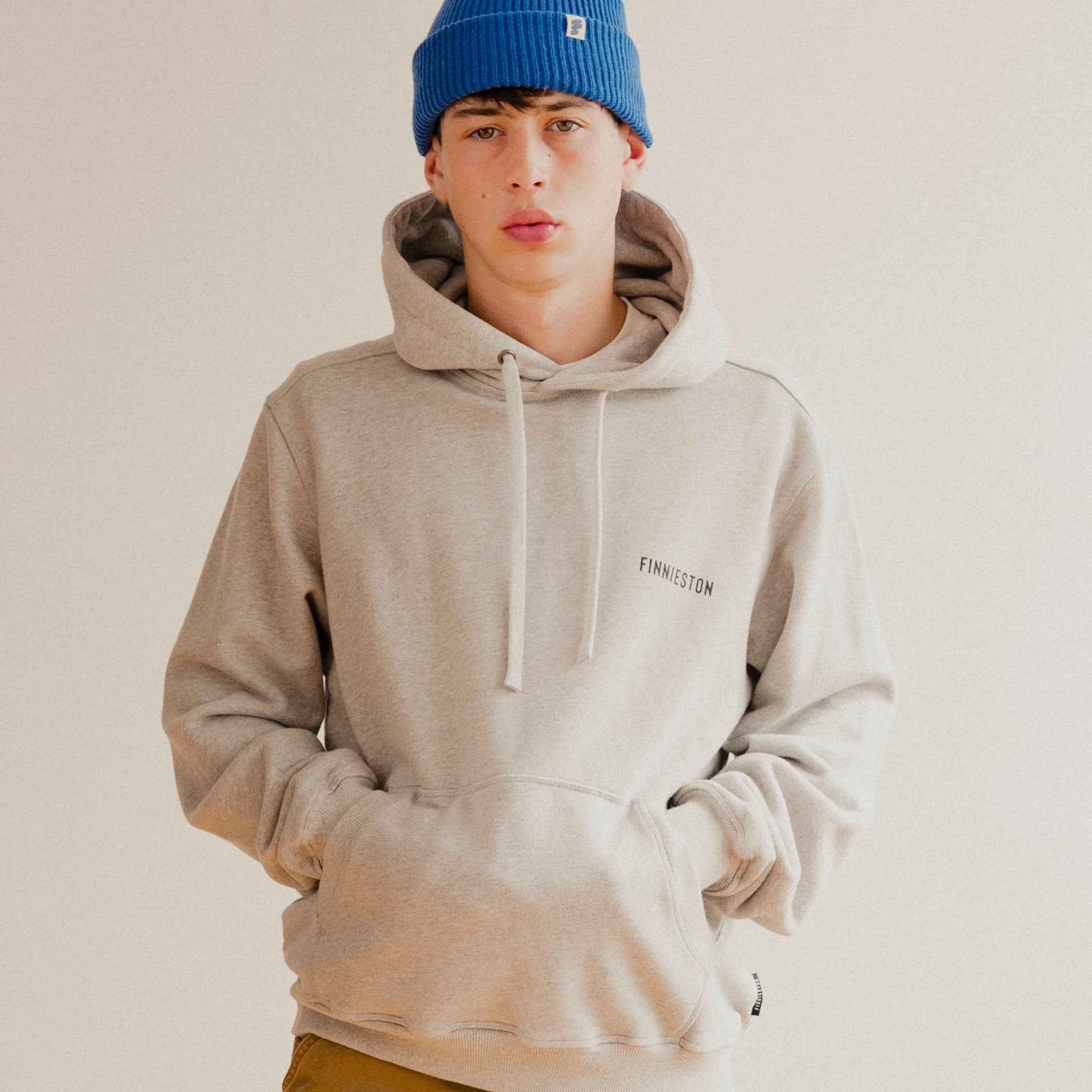 Person wearing a grey hoodie and blue beanie on a plain background