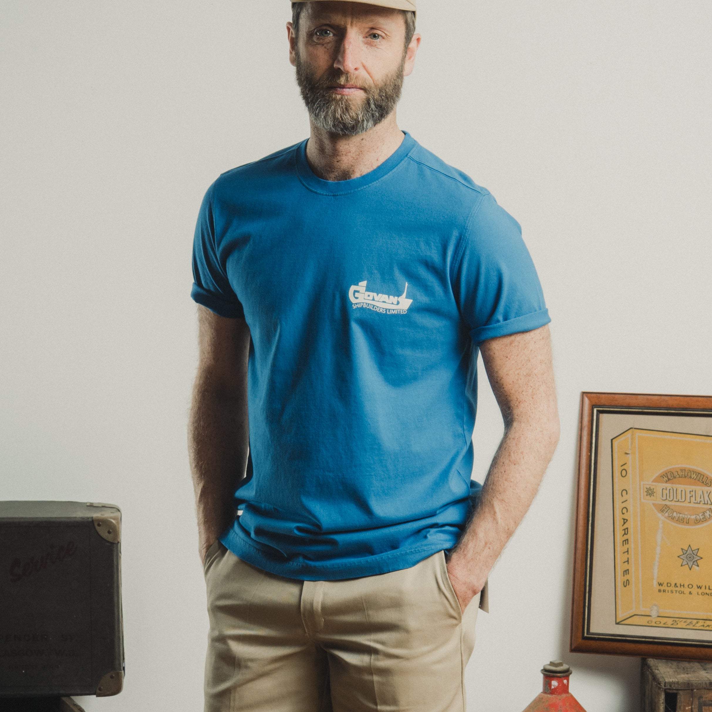 Man wearing a blue t-shirt with a logo, standing in a room with vintage items.
