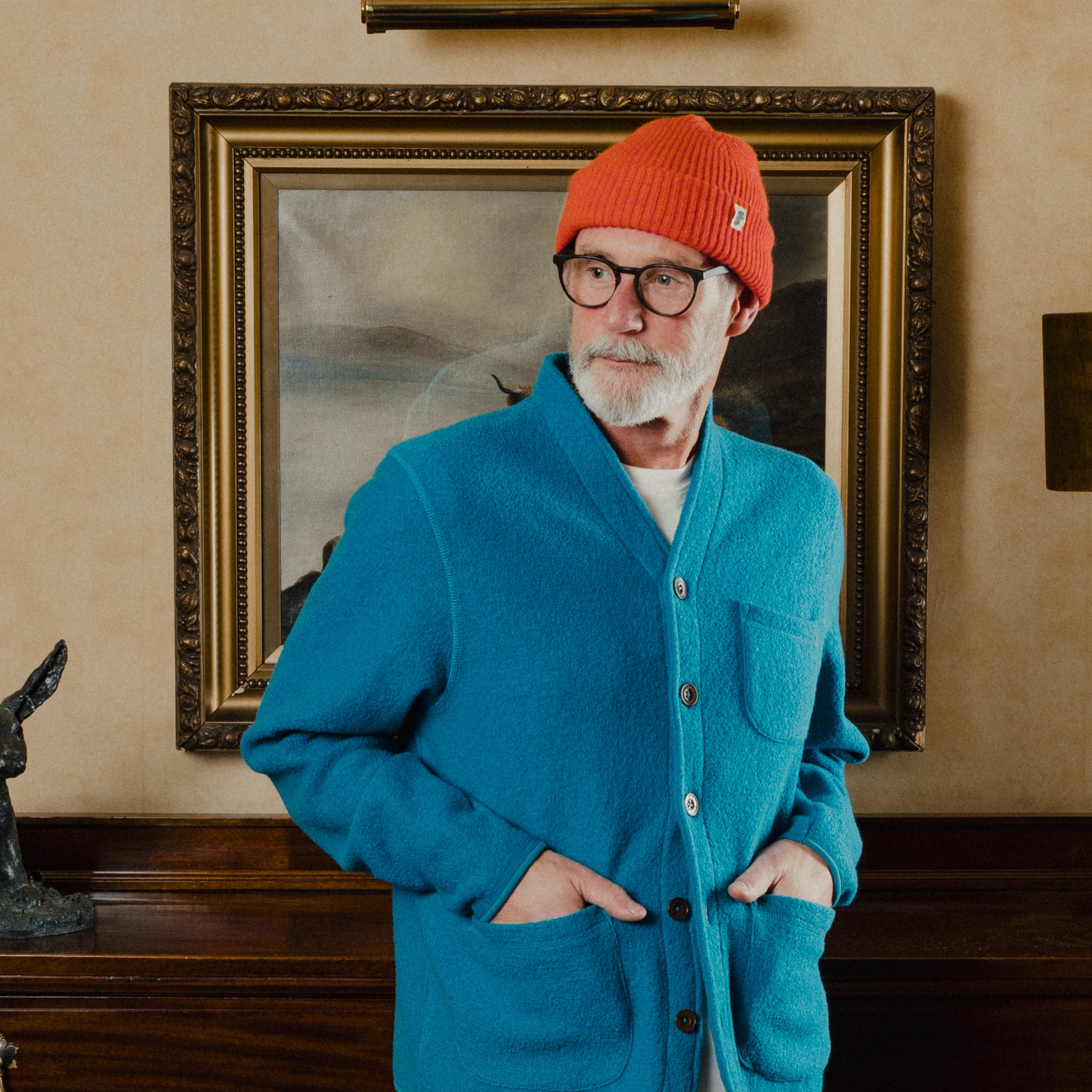 Man wearing a blue jacket and orange beanie standing in front of a painting