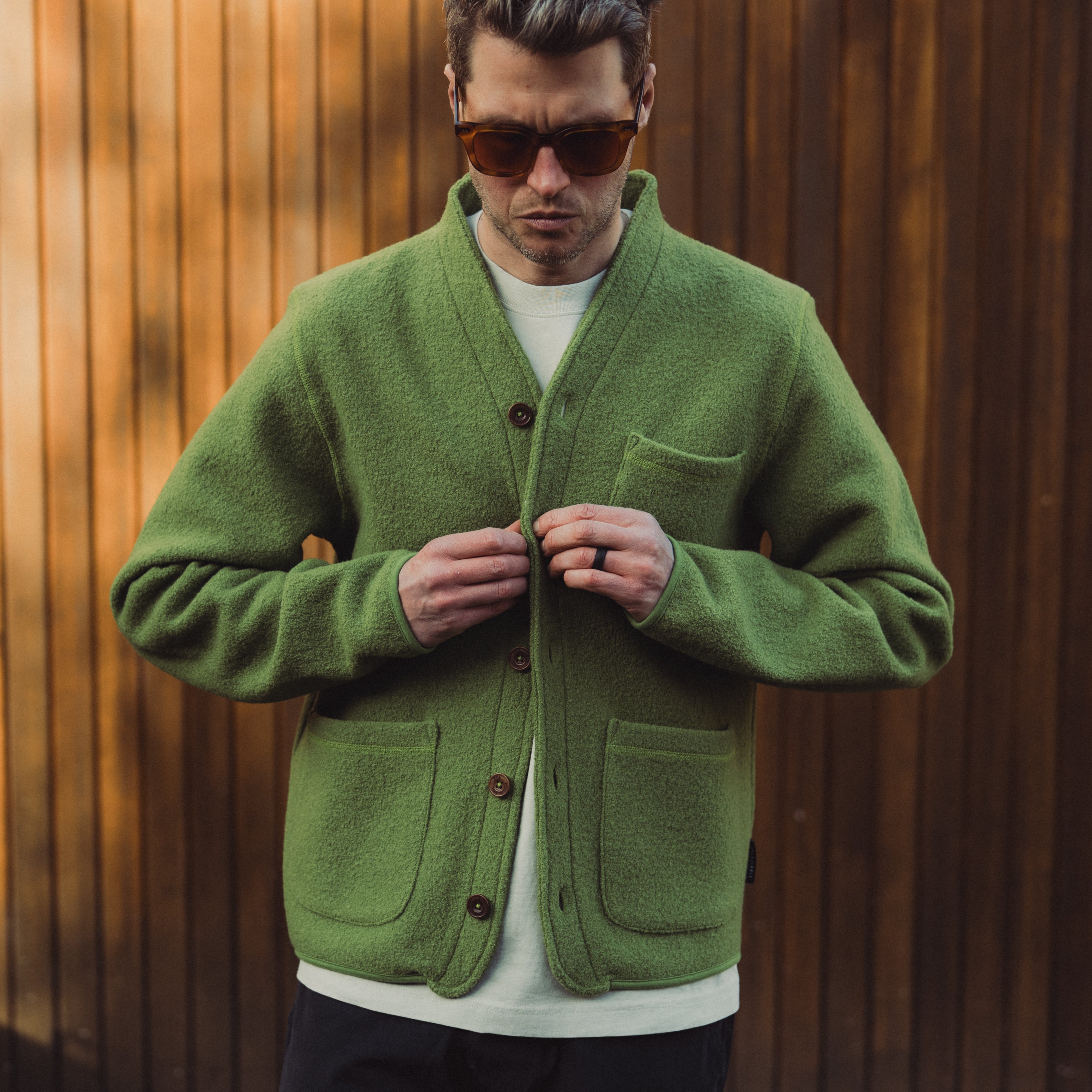 Man wearing a green cardigan against a wooden background