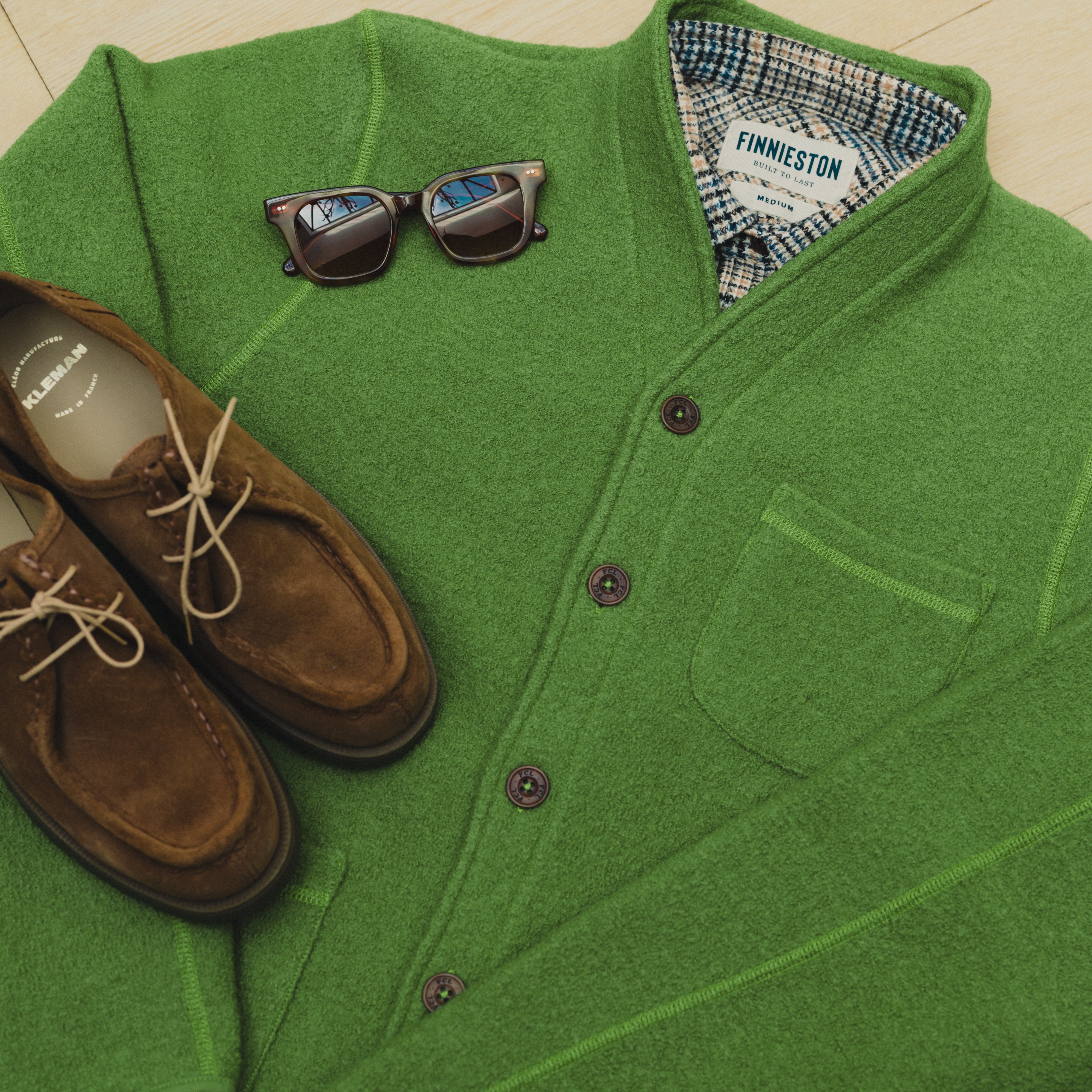 Green cardigan with sunglasses and brown shoes on a light background