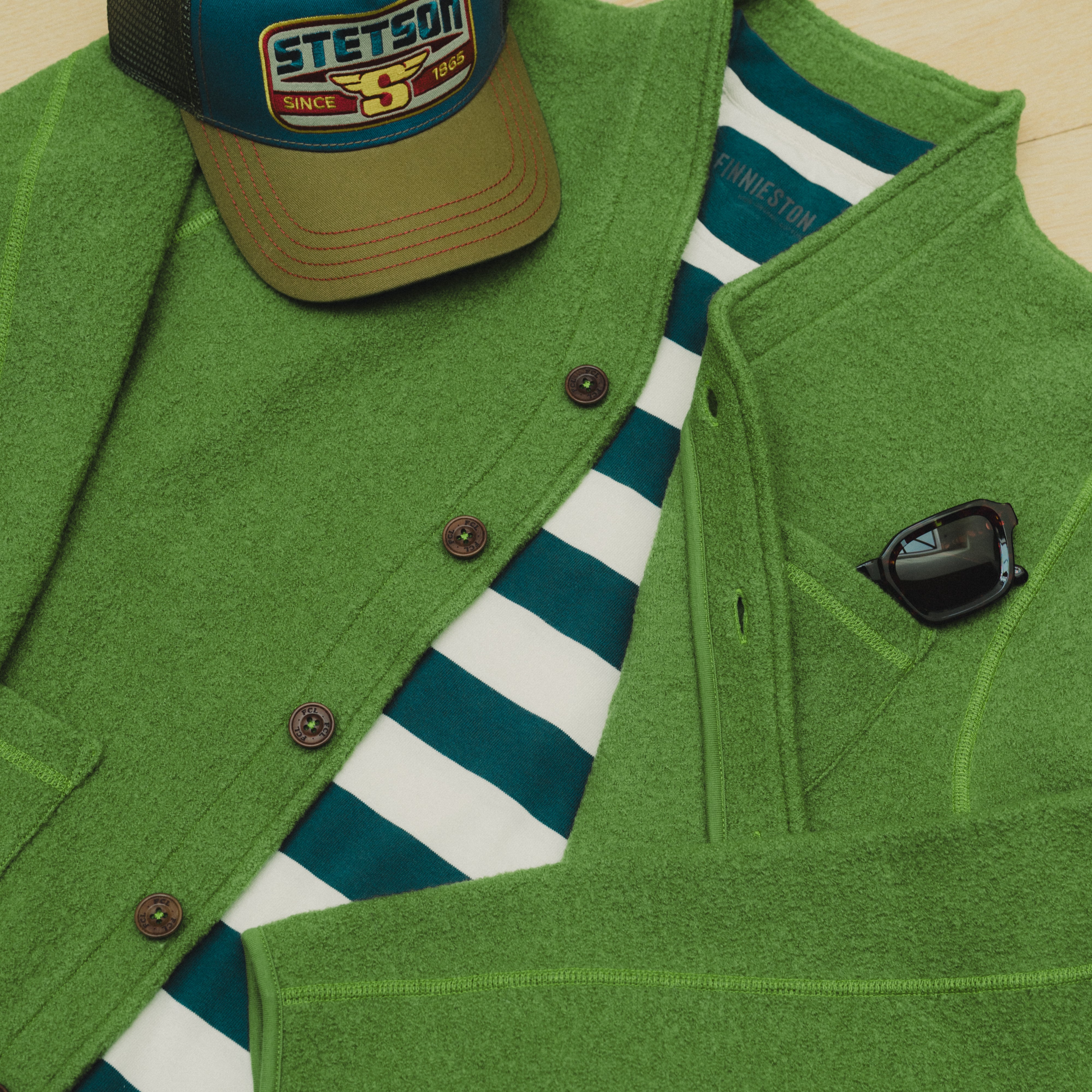 Green jacket, striped shirt, and cap with Stetson logo on a wooden surface