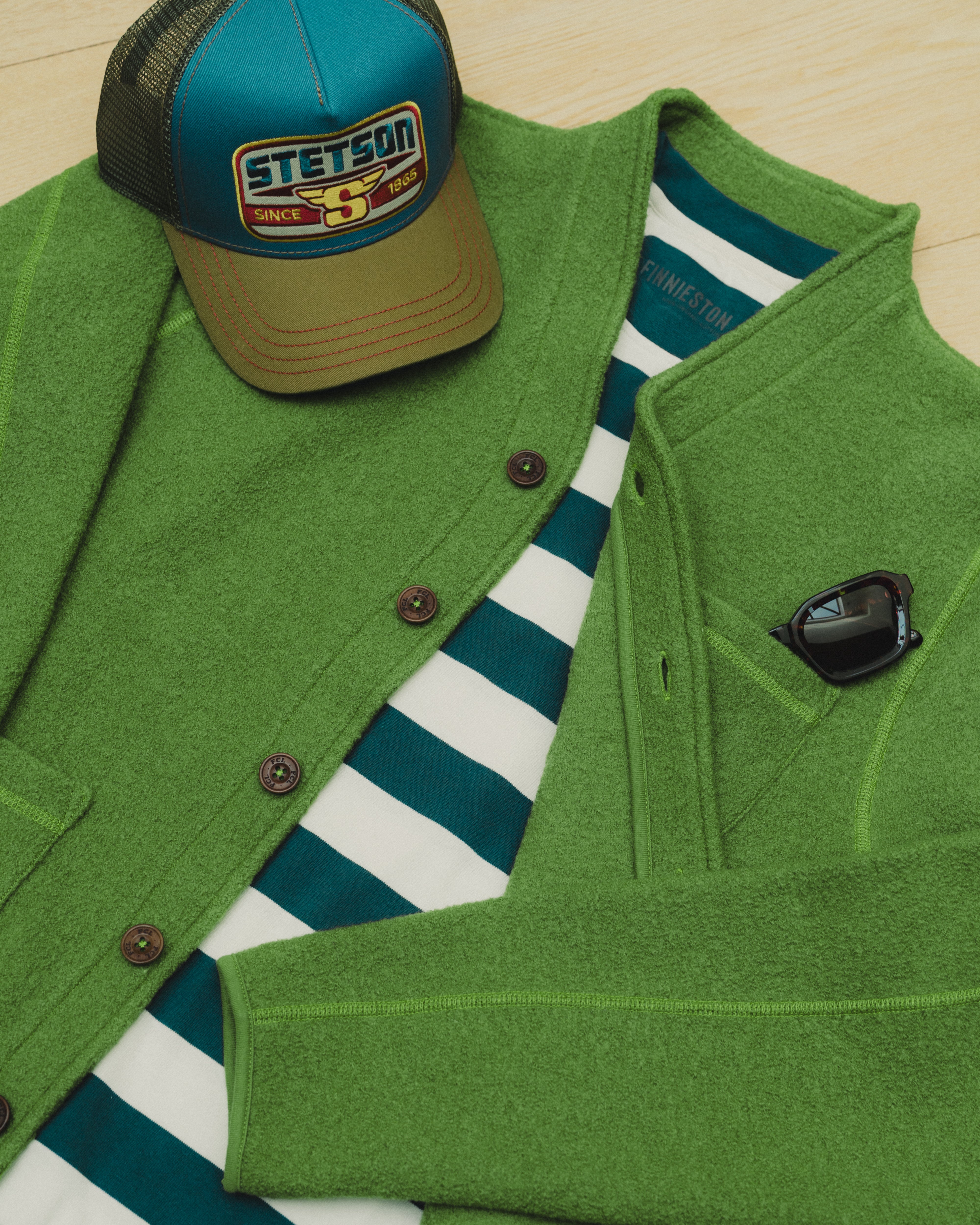 Green jacket, striped shirt, and cap with Stetson logo on a wooden surface