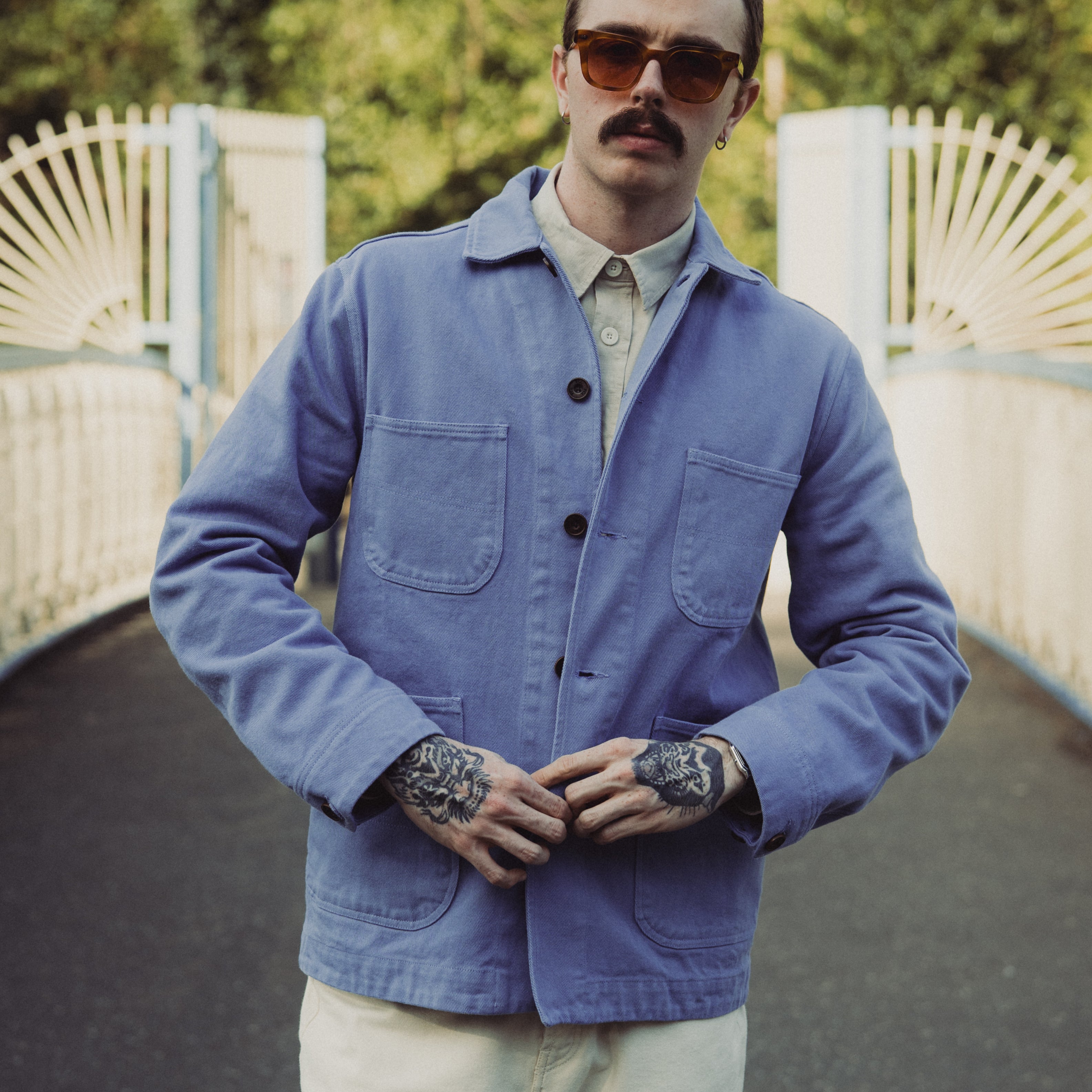 Man wearing a blue jacket and sunglasses standing outdoors with a blurred background