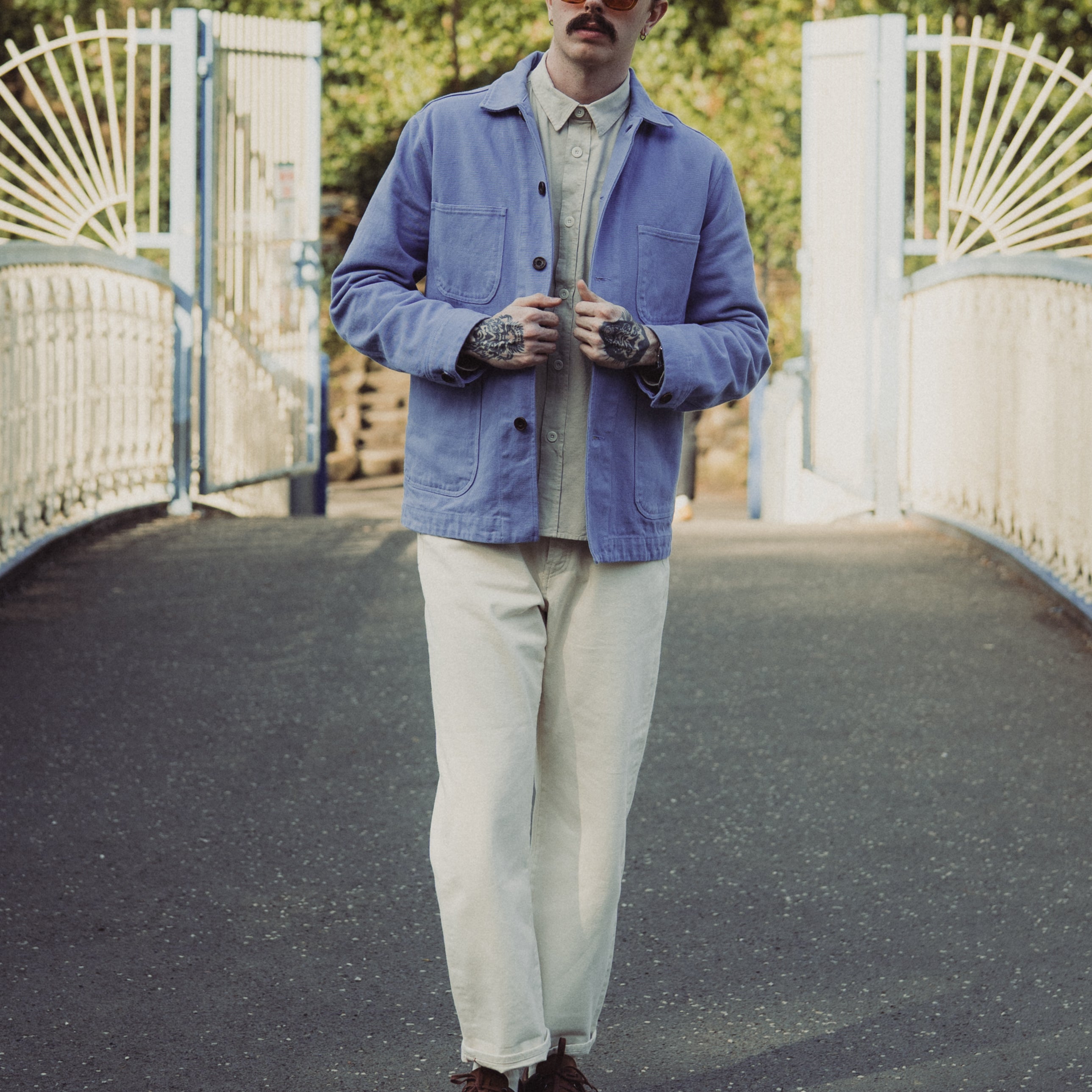 Man wearing a blue jacket and sunglasses standing on a bridge