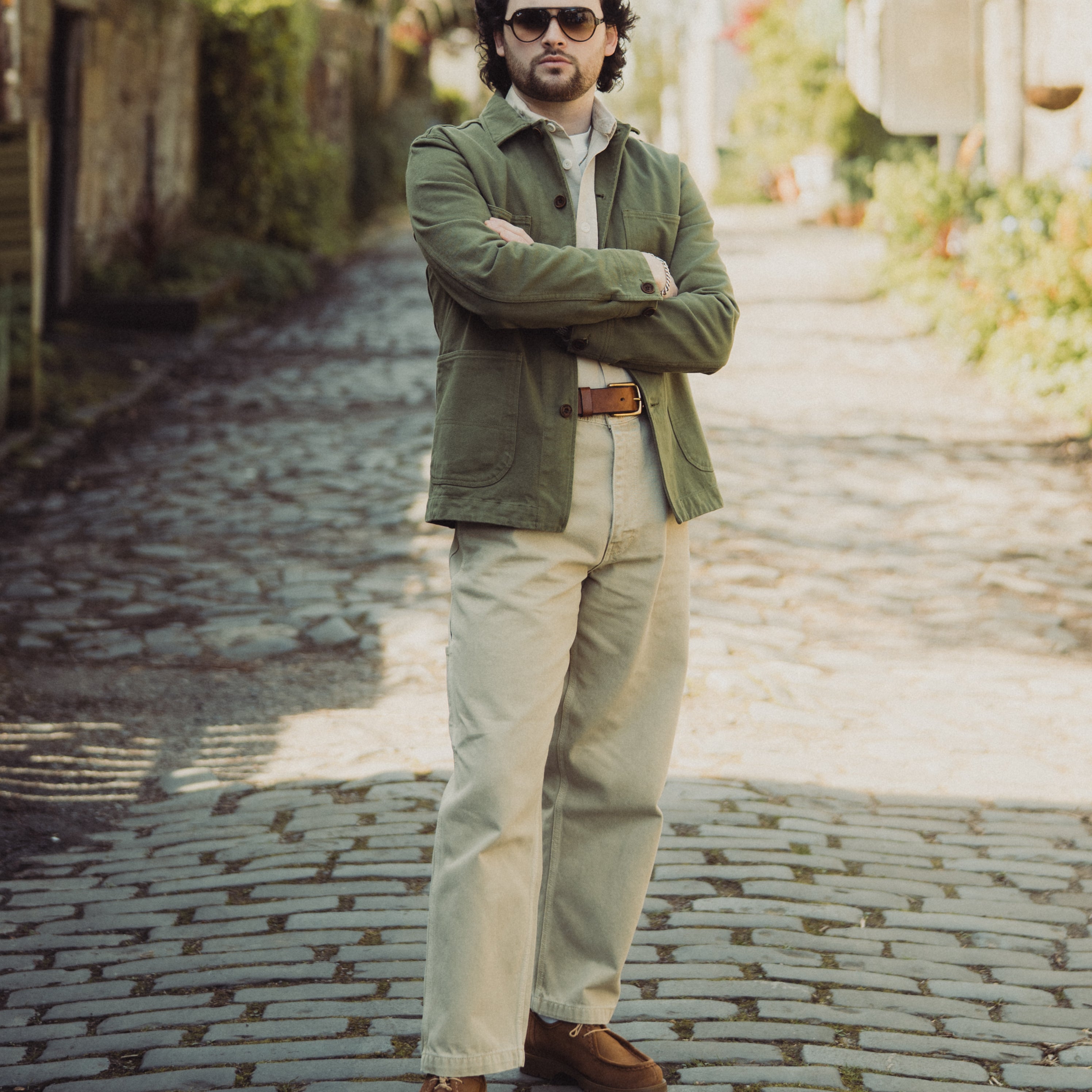 Man standing on a cobblestone street wearing a green jacket and sunglasses.