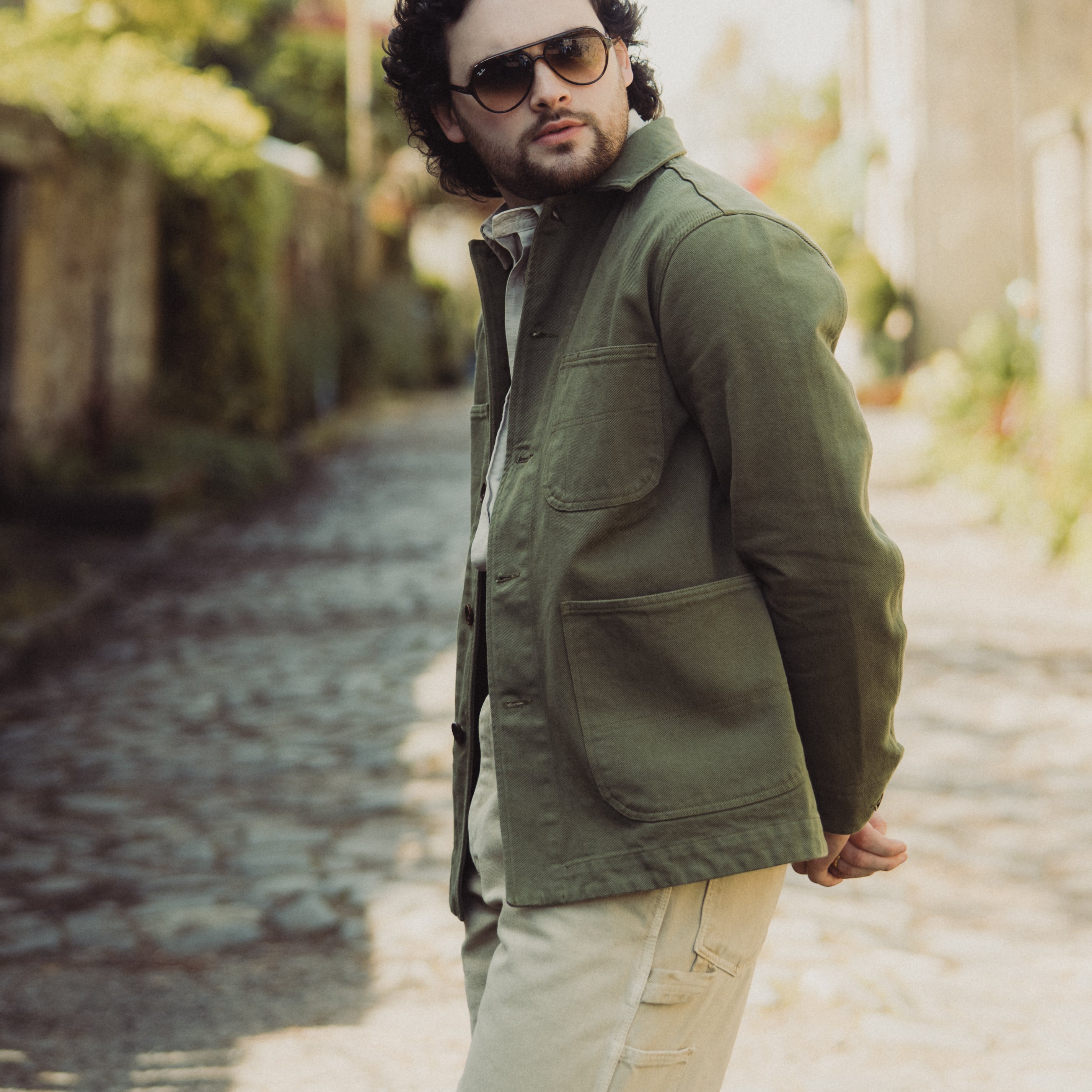Man wearing a green jacket and sunglasses on a blurred street background