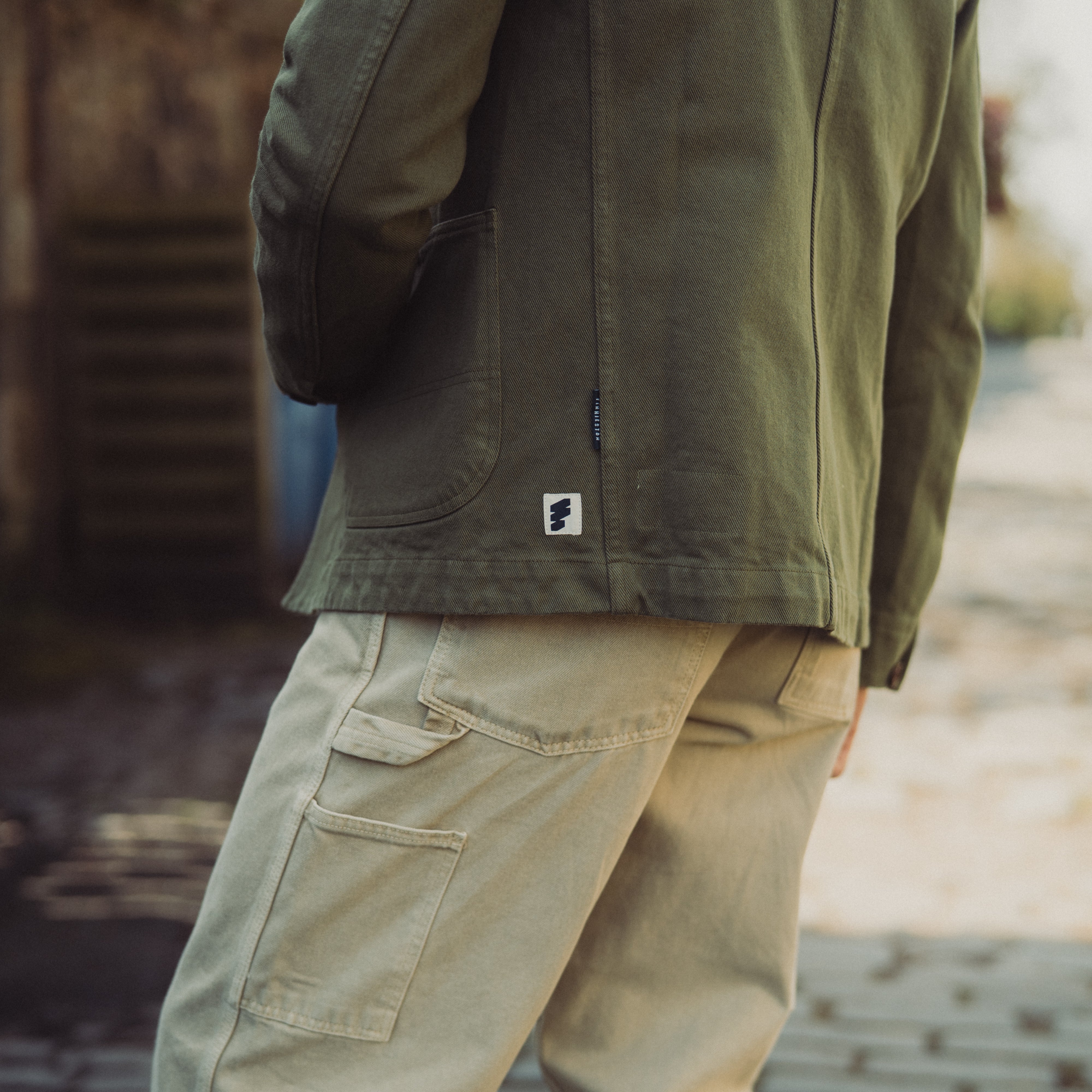 Person wearing a green jacket and beige pants on a blurred outdoor background