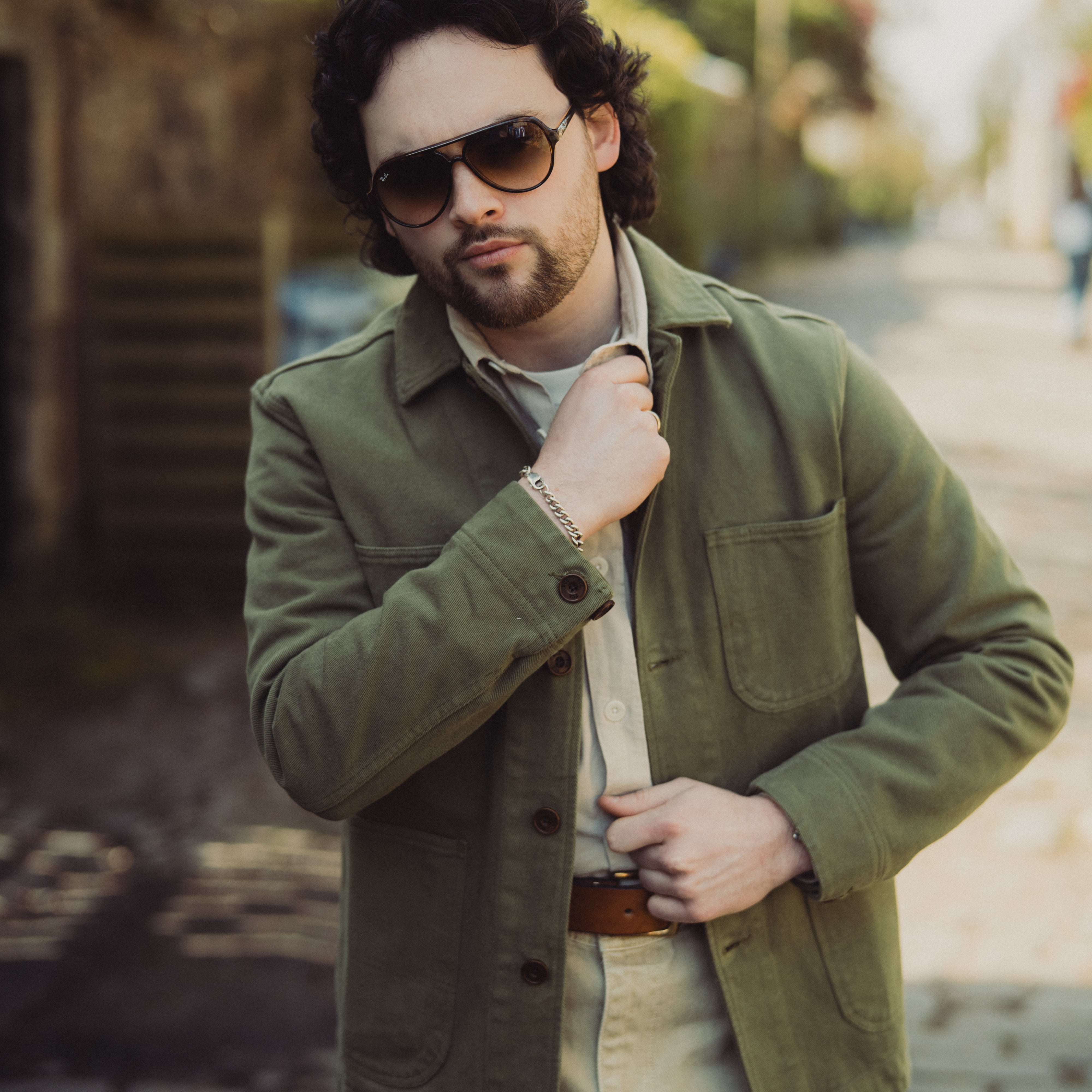 Man wearing a green jacket and sunglasses on a blurred street background