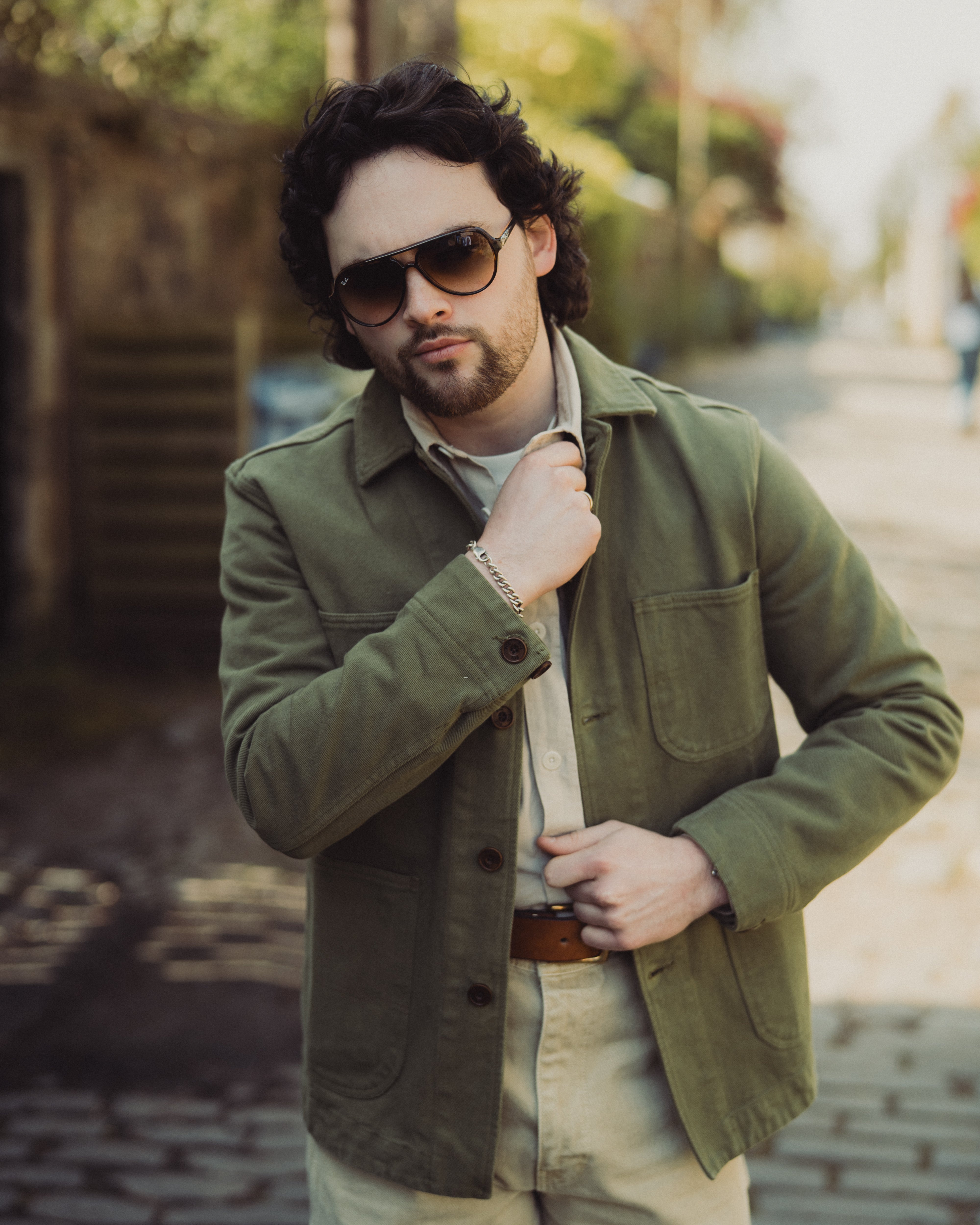 Man wearing a green jacket and sunglasses on a blurred street background